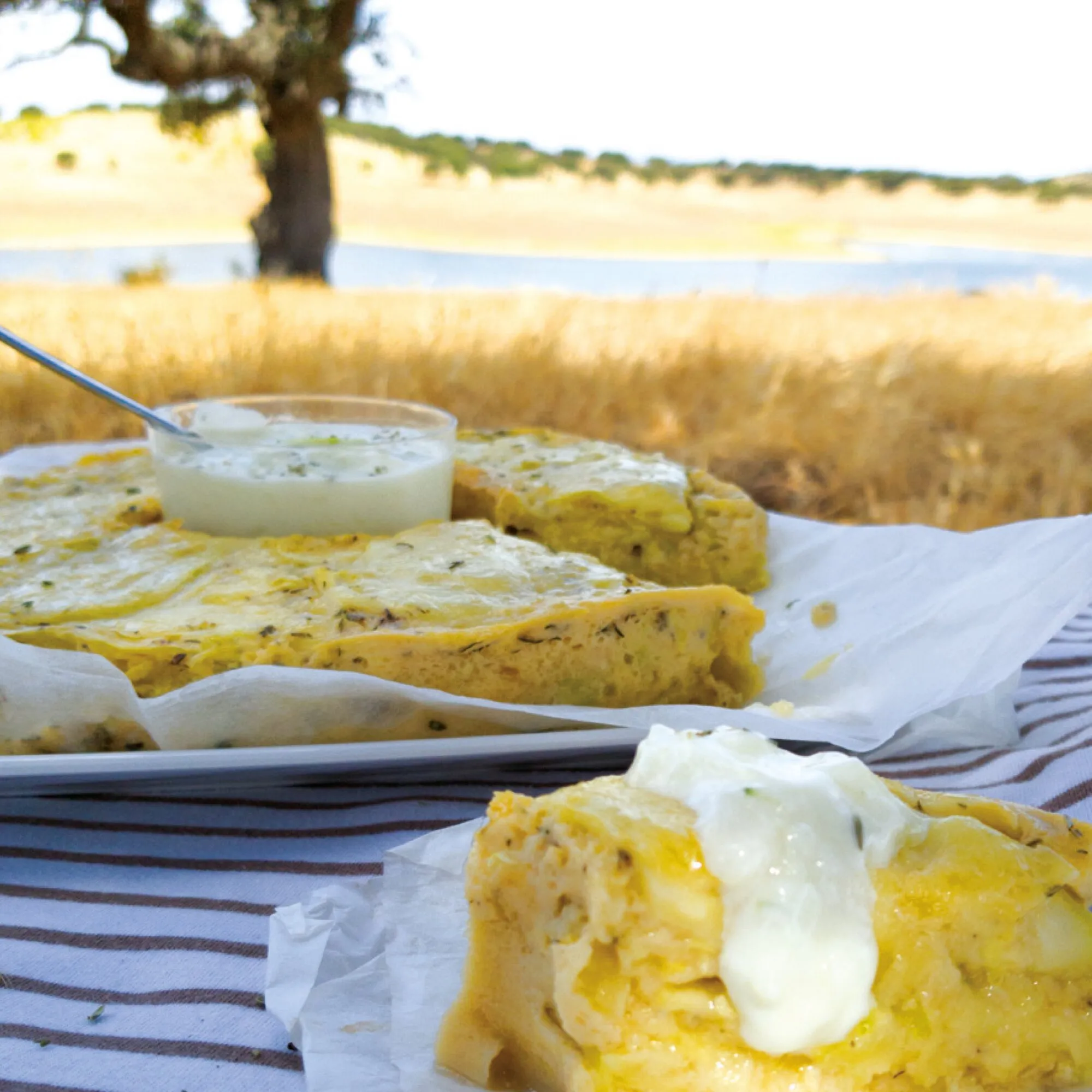 Herzhafte Quiche-Stücke mit Kräutern und Sauerrahm auf Backpapier vor Dünen und See, Motiv zum Kochbuch Auflauf, Quiche, Pizza & Co.