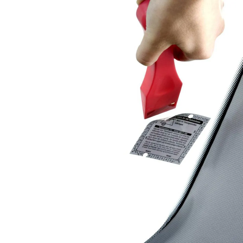 Roter Vignettenschaber wird an einer Autoscheibe neben einer entfernten Umweltplakette angesetzt