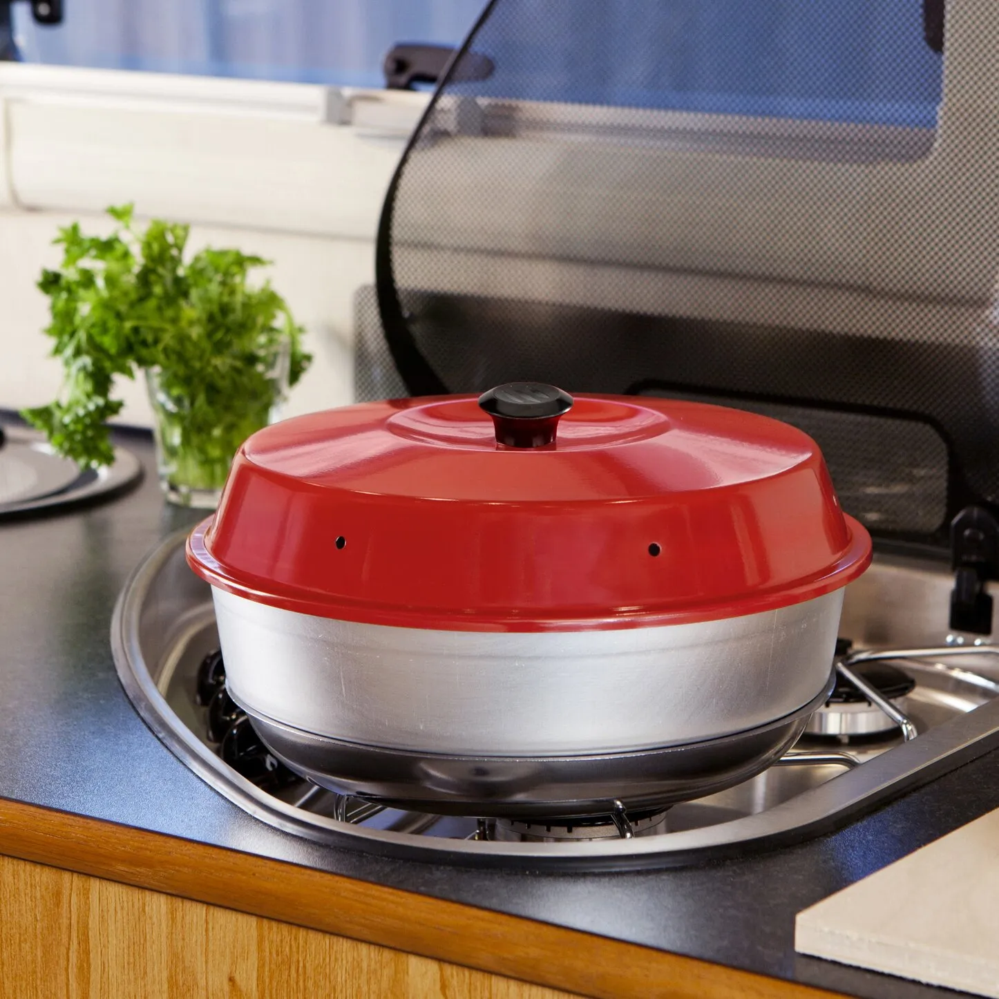 Roter Classic-Backofen mit schwarzem Deckel auf einem Herd, daneben frische Petersilie in der Küche