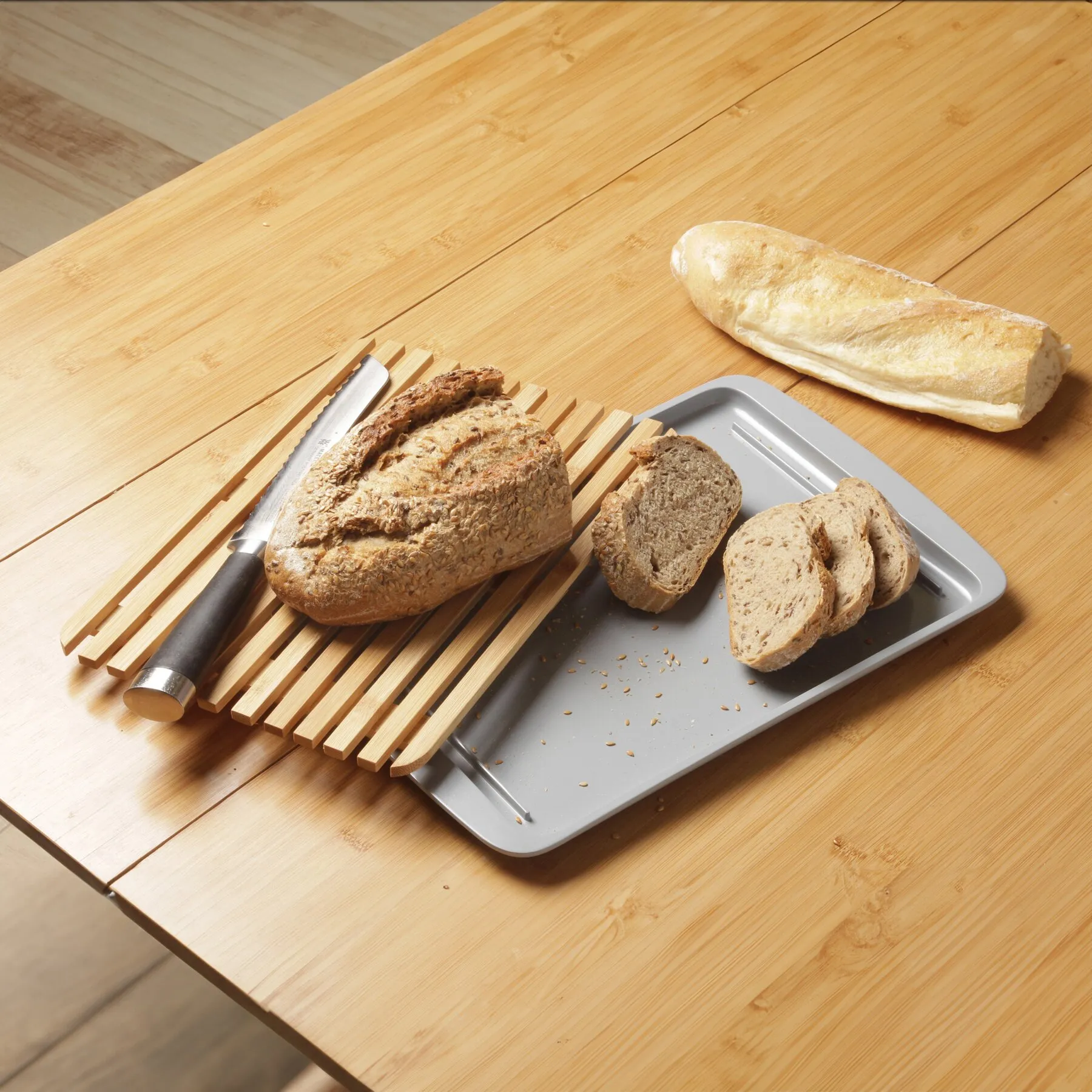 Graues Schneide- und Servierbrett mit Holzleisten, Brotmesser und verschiedenen Brotscheiben auf einem Holztisch