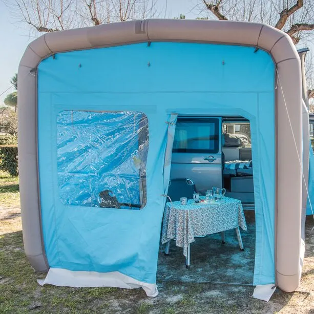 Blaue Frontwand der Camping GT Box mit aufblasbarem grauem Rahmen, Fenster und Eingang zum Wohnbereich mit gedecktem Tisch