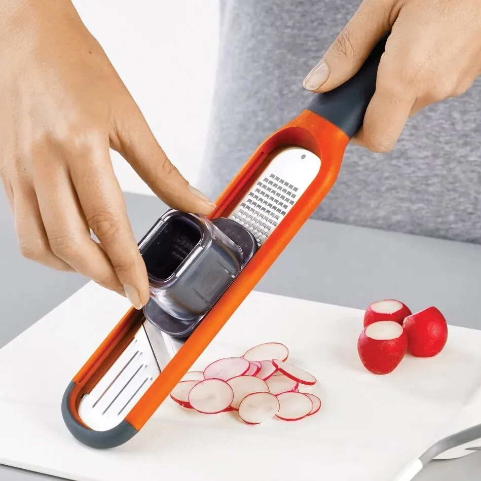 Orange Minireibe mit Fingerschutz beim Hobeln von Radieschen auf einem Schneidebrett