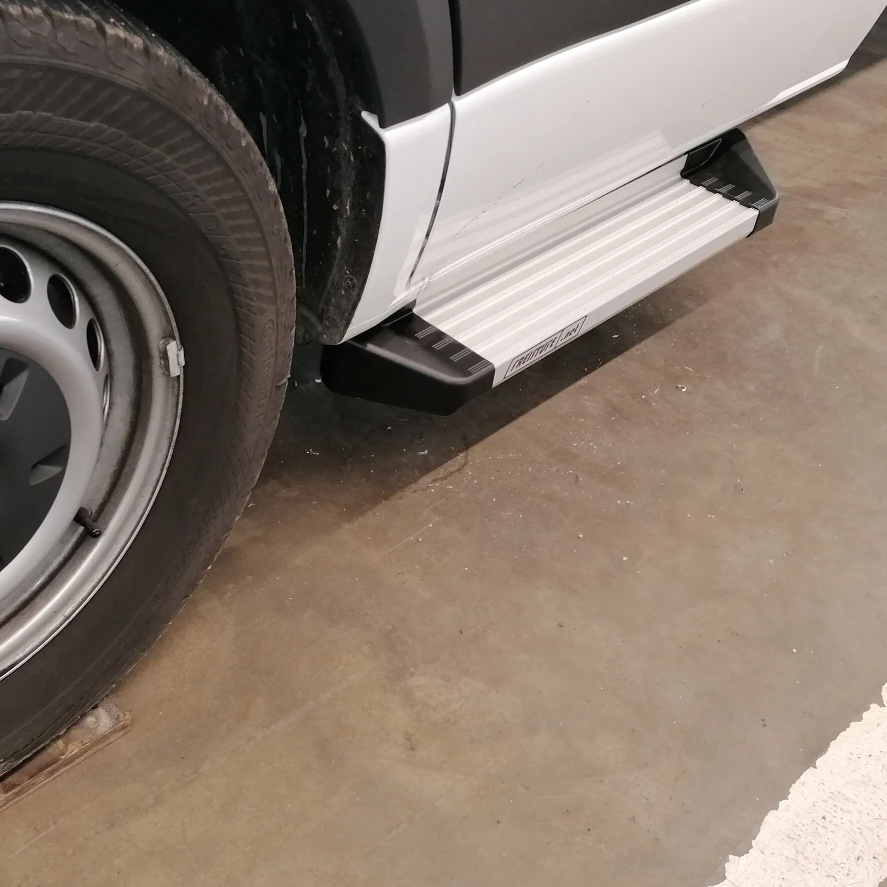 Silberne Freistufe mit geriffelter Trittfläche und schwarzen Endkappen am weißen Mercedes Sprinter oder VW Crafter ab 2006