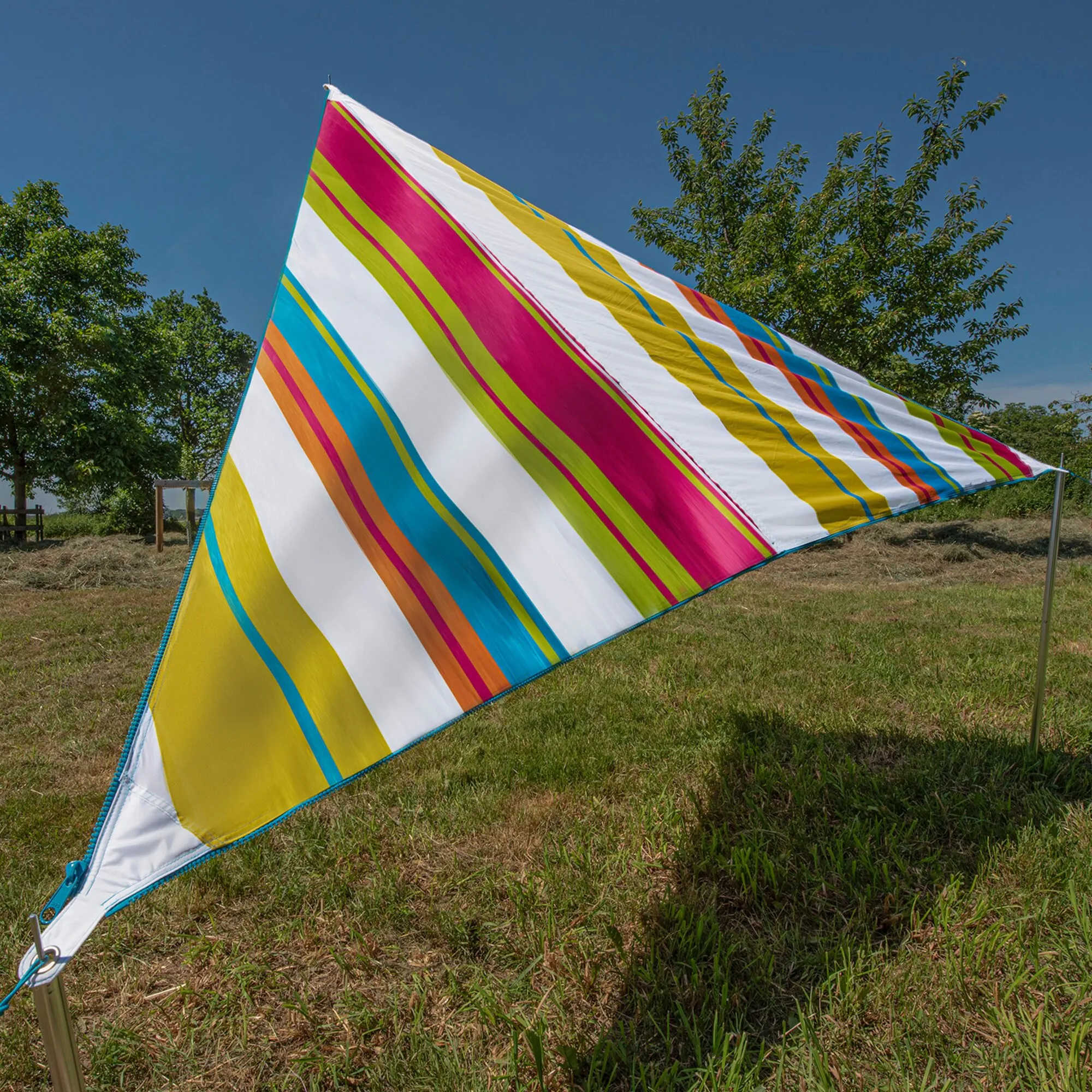 Bunt gestreiftes dreieckiges Sonnensegel Zip Canvas Caribbean auf einer Wiese zwischen Metallmasten gespannt, mit Befestigungsösen an den Ecken