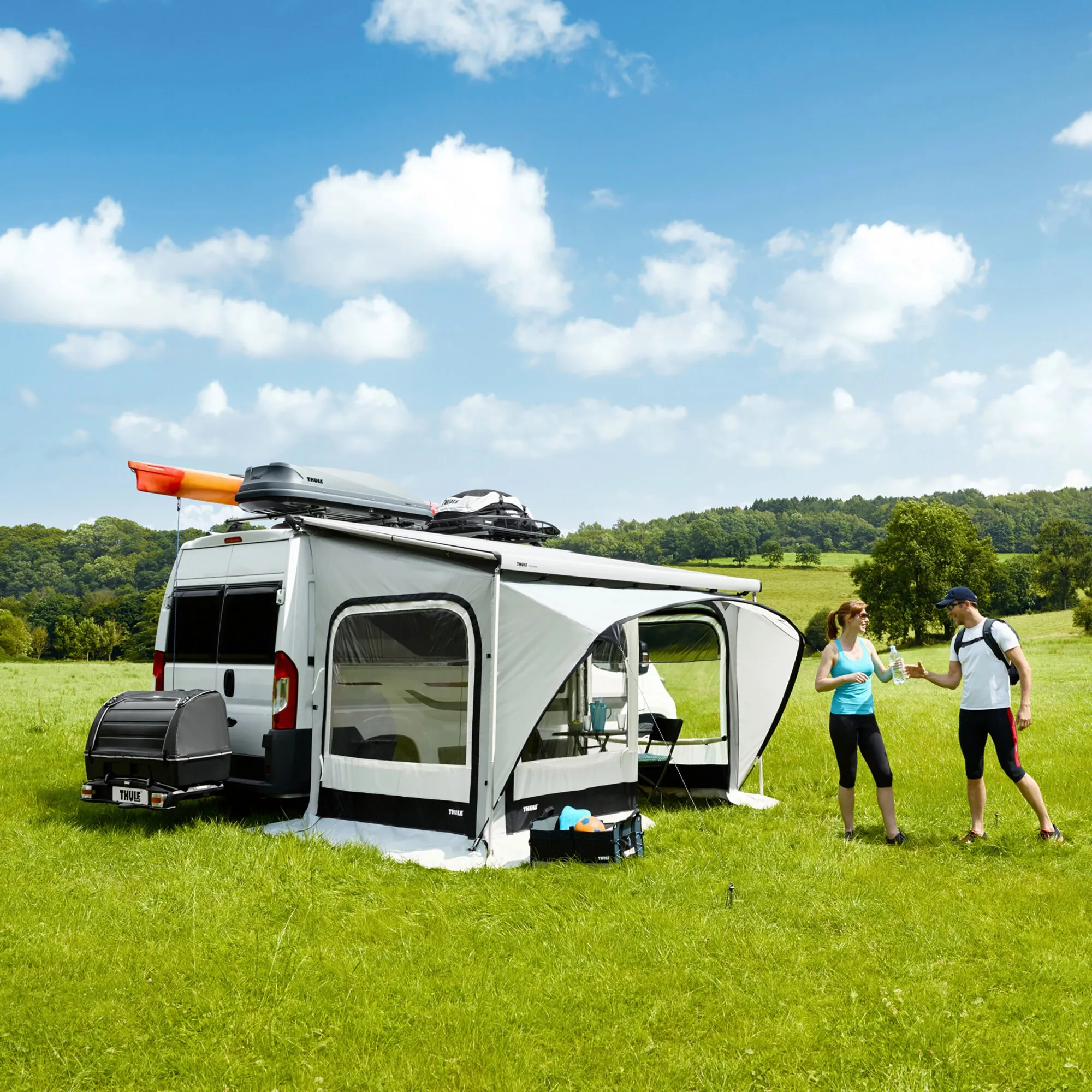 Weißer Kastenwagen mit aufgebautem Thule QuickFit Ducato Markisenzelt und zwei Personen auf einer grünen Wiese