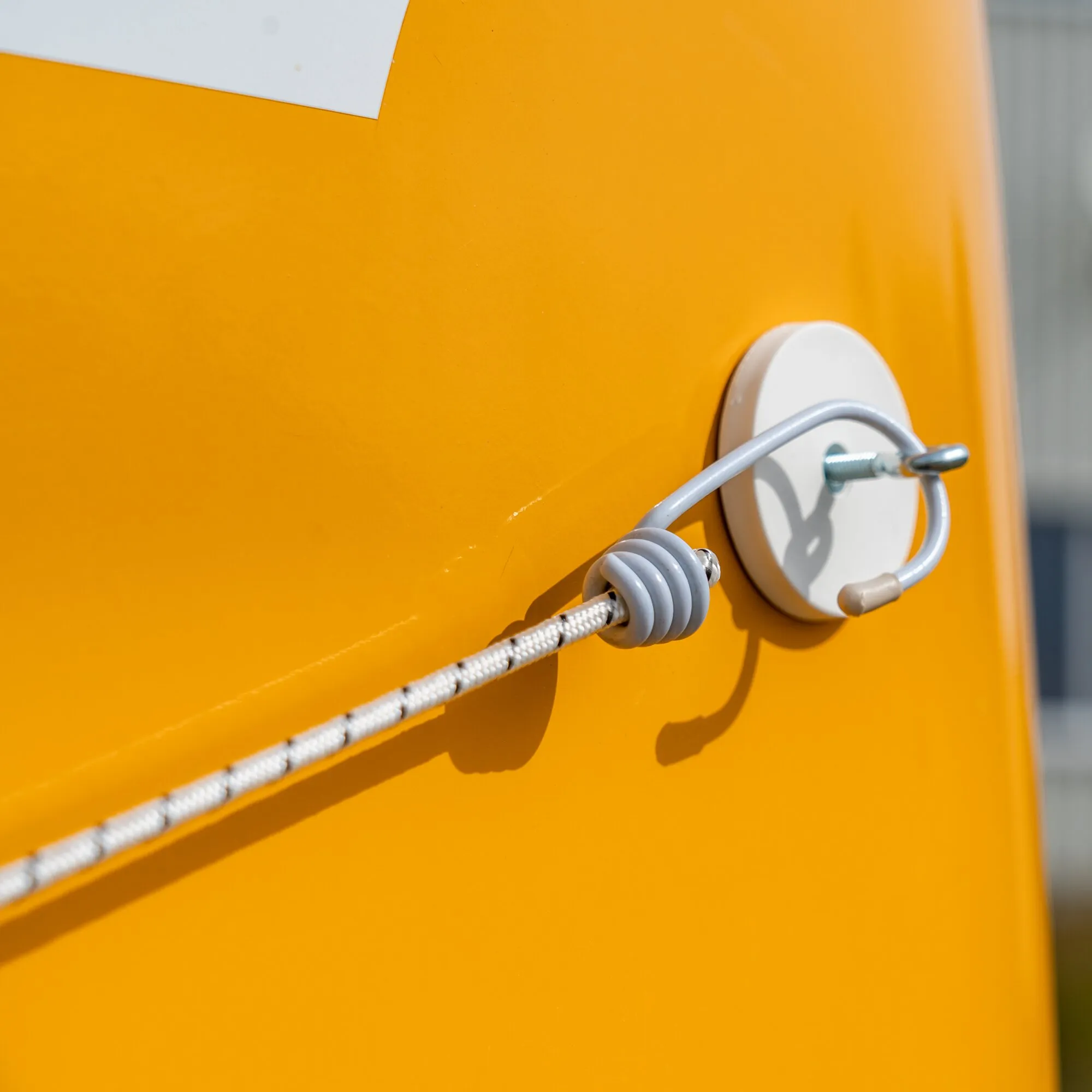 Detailaufnahme eines weißen Magnet-Sets Classic mit Seil und Metallhaken an einer orangefarbenen Fläche