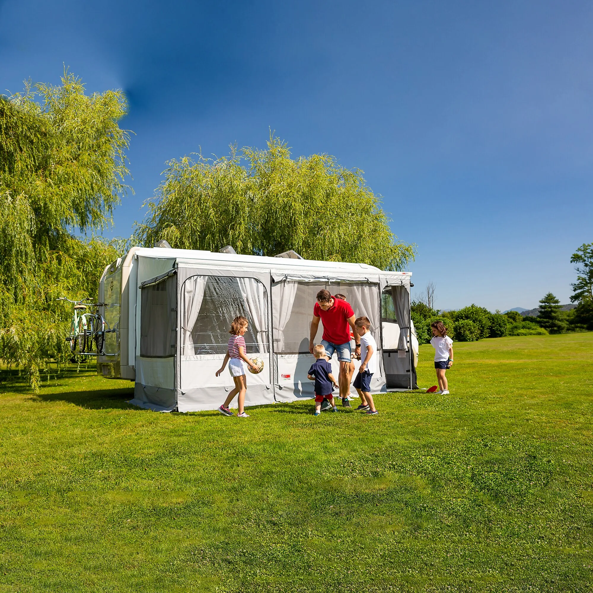 Graues Markisenzelt Privacy Room F45, 300 Large an einem Wohnwagen, während eine Familie davor auf der Wiese spielt