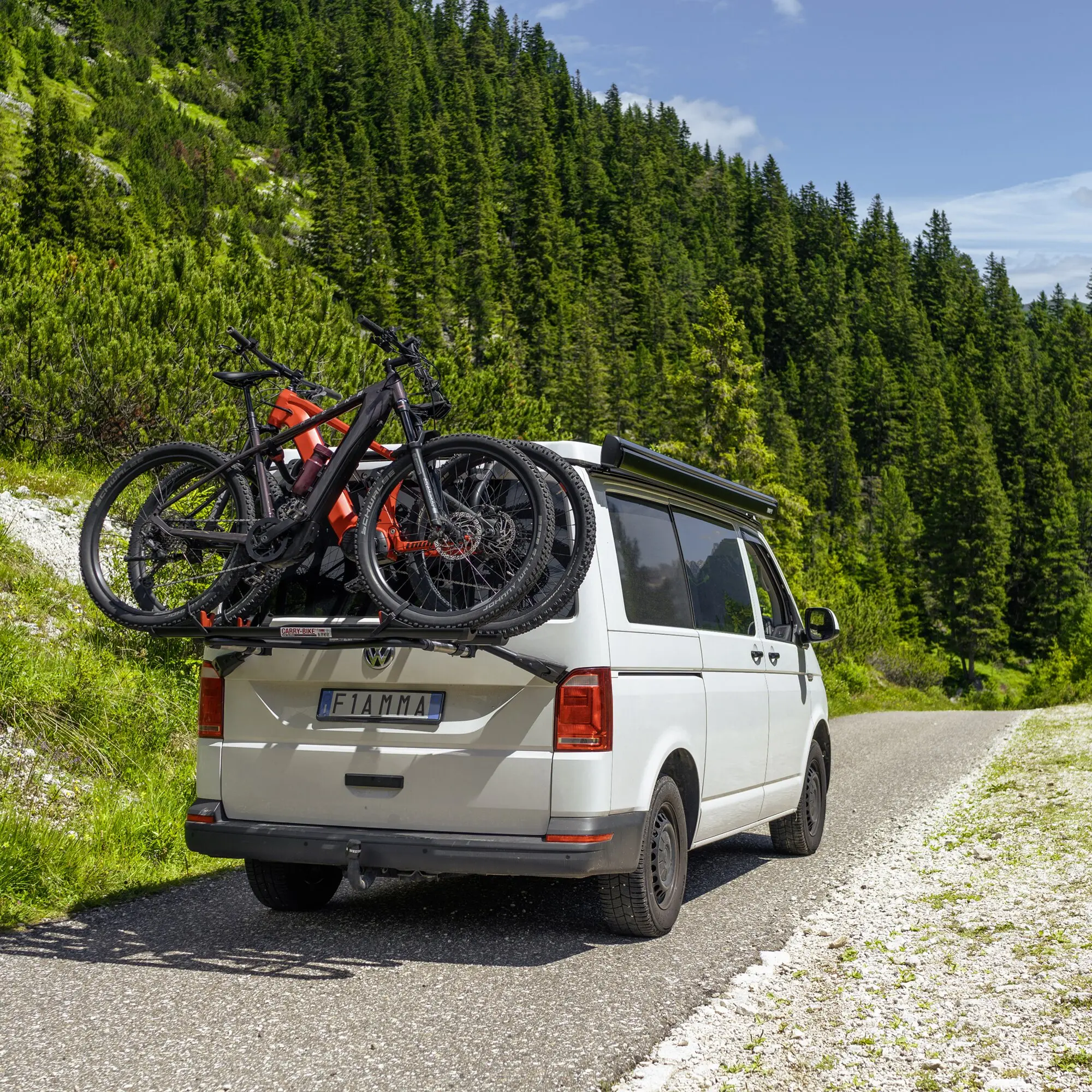 Auf dem Heck eines weißen VW Transporter befestigter Carry-Bike VW T6 Pro Deep Black Fahrradträger mit zwei Mountainbikes, Berglandschaft im Hintergrund