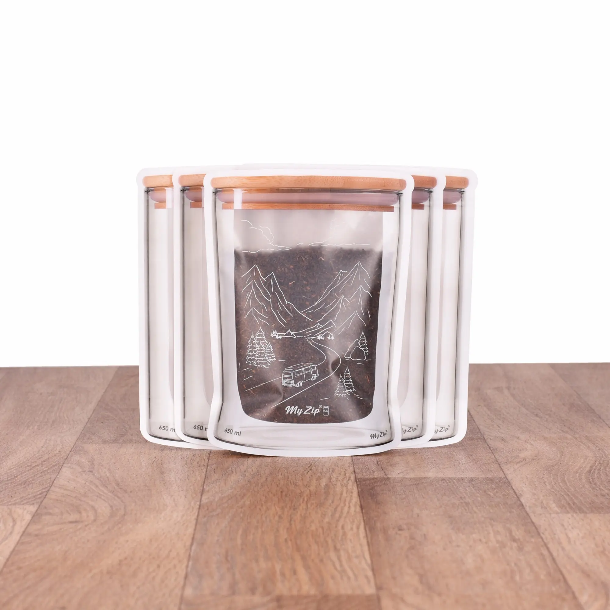 Fünf transparente Aufbewahrungsbeutel mit weißem Rand und Holzdeckel, brauner Inhalt sichtbar, Vorderseite zeigt Berglandschaft mit Bäumen und Straße, 650 ml