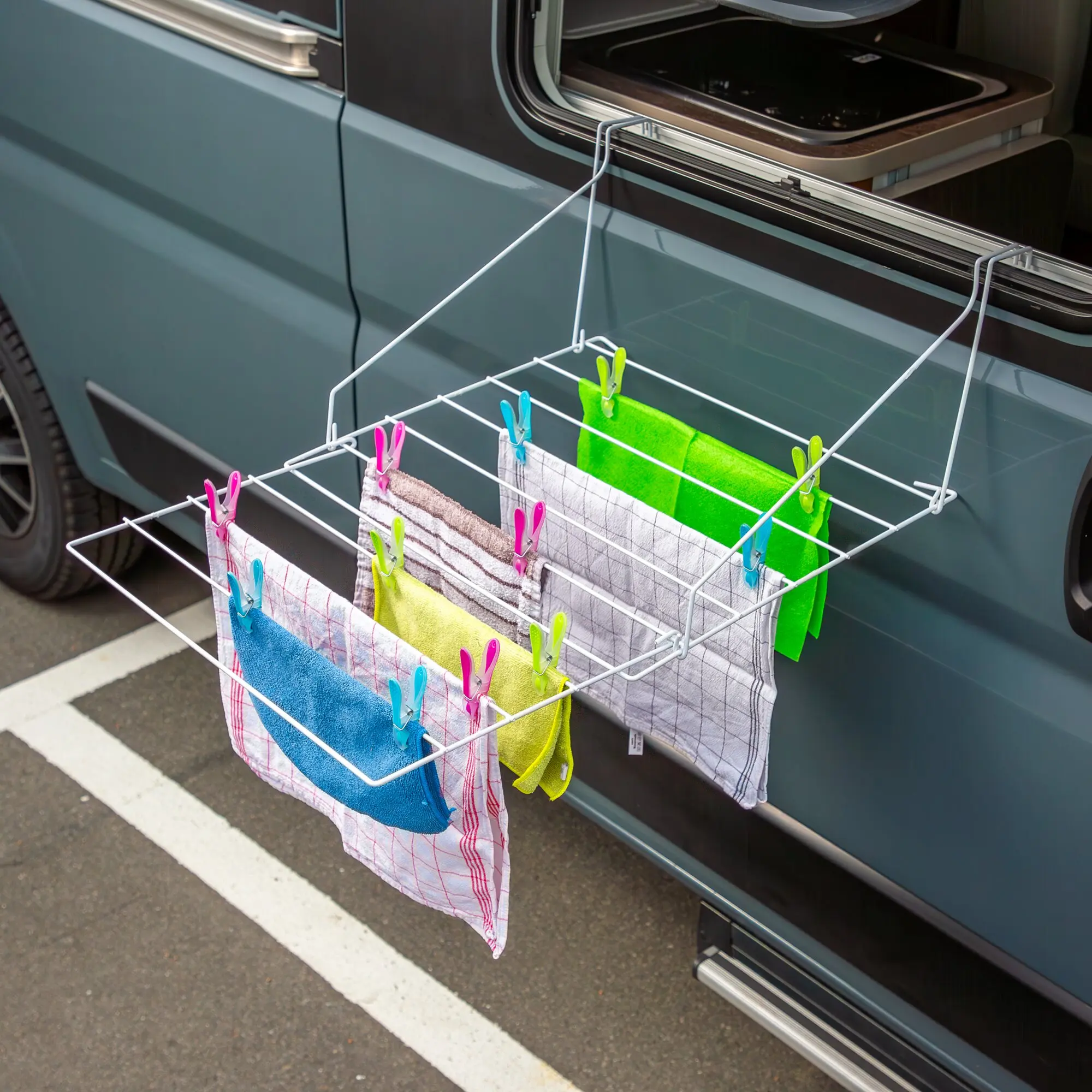 Seitliche Aufnahme eines blauen Vans mit offener Tür; ein weißer Wäscheständer hängt aus dem Türrahmen, darauf bunte Handtücher und Wäscheklammern