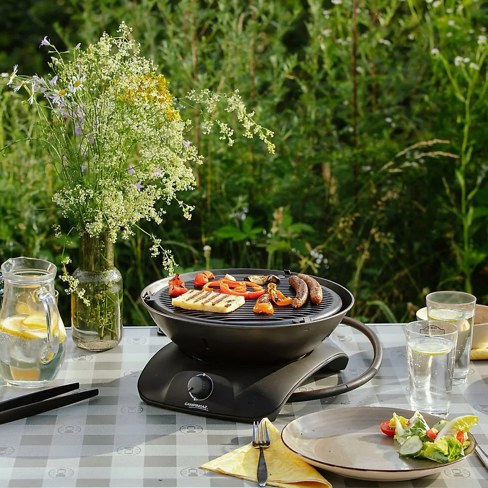 Schwarzer Tischgrill 360 Grill CV mit Grillrost, Würstchen und Gemüse auf einem gedeckten Gartentisch