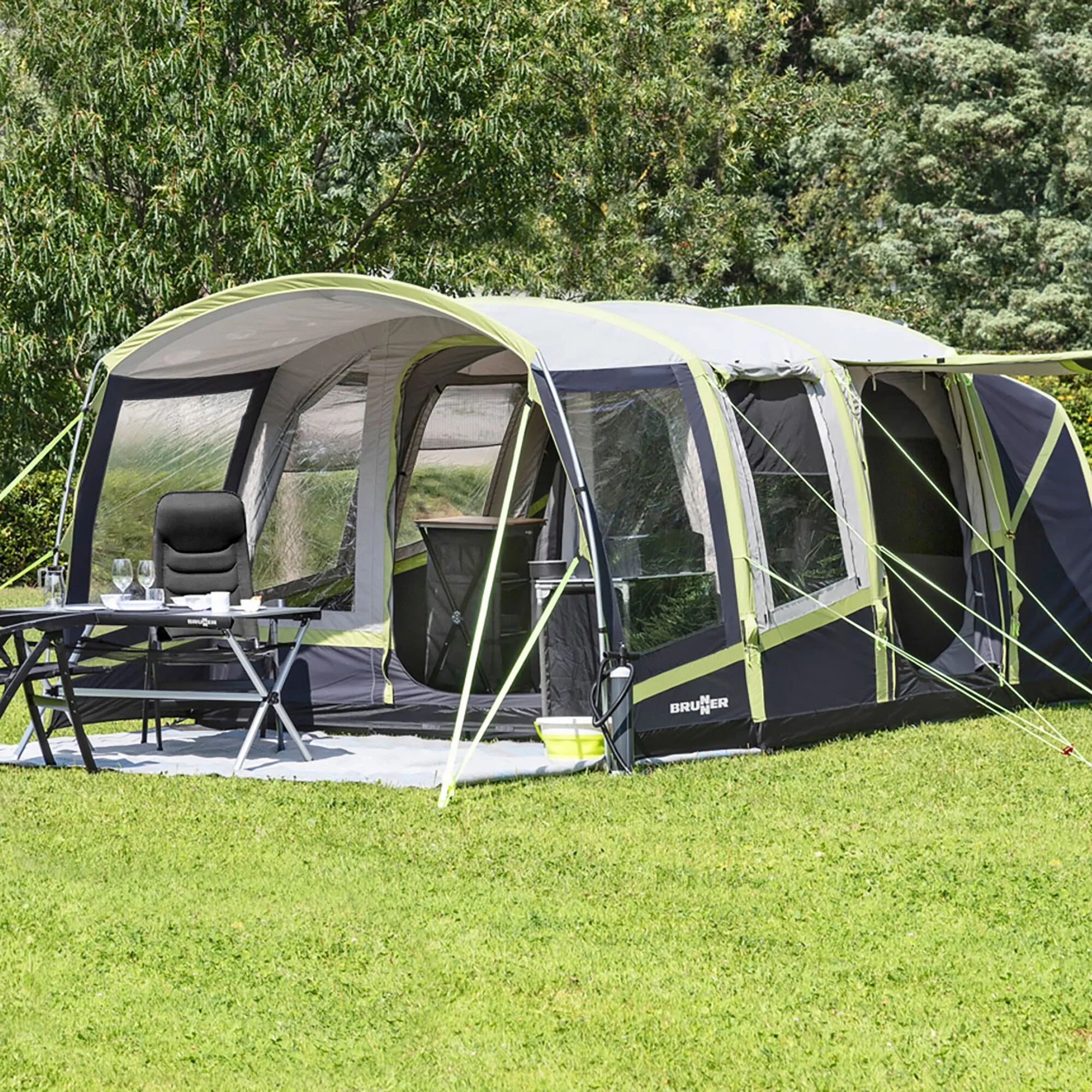 Aufgebautes Zelt Pure 4 von Brunner in Dunkelblau, Grau und Grün mit geöffnetem Vorraum, Campingtisch und Stühlen auf einer Wiese