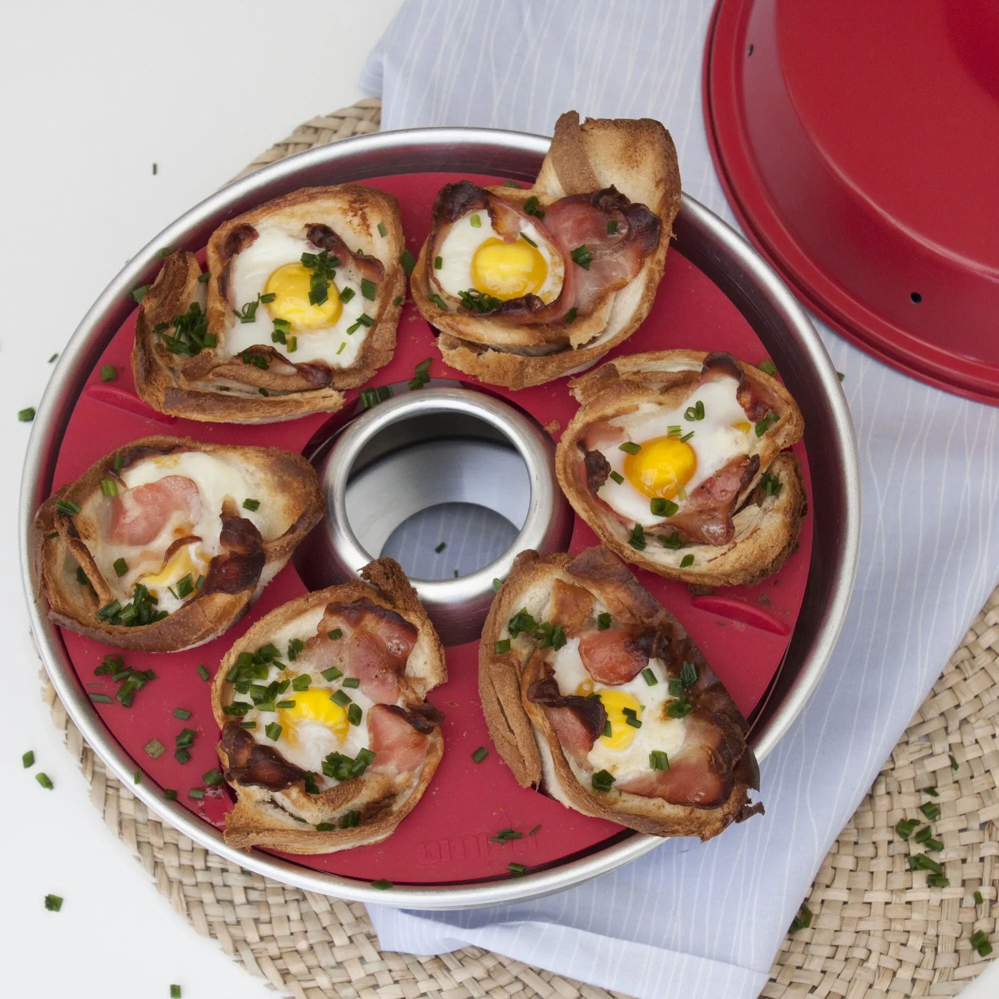 Roter Omnia Backofen mit gerösteten Brotscheiben, Spiegeleiern, gebratenem Speck und Schnittlauch in der Backform