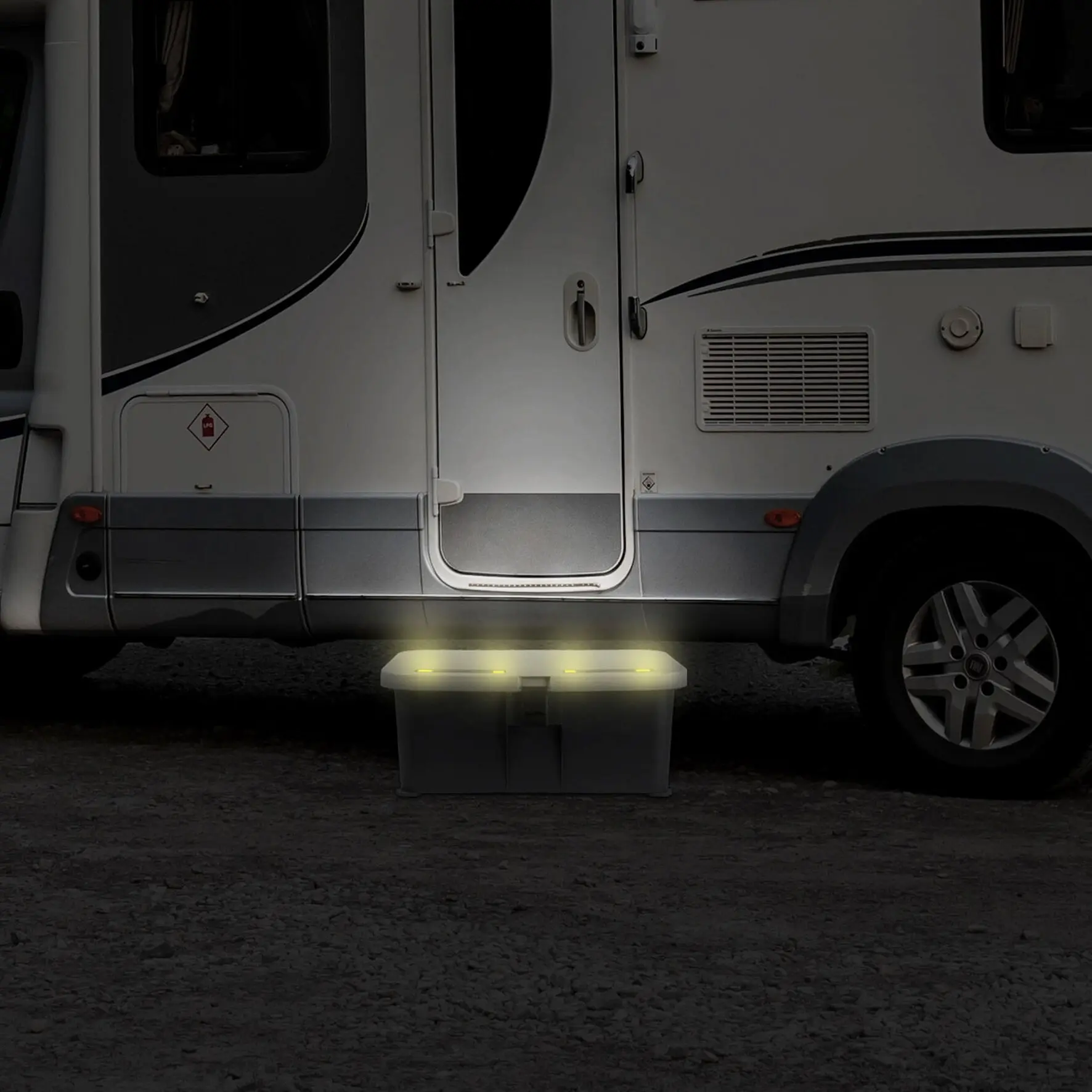 Trittstufe Boxstep NG vor der Wohnmobil-Tür, rechteckige weiße Kunststoffstufe mit integrierten gelb leuchtenden LEDs, dunkler Hintergrund