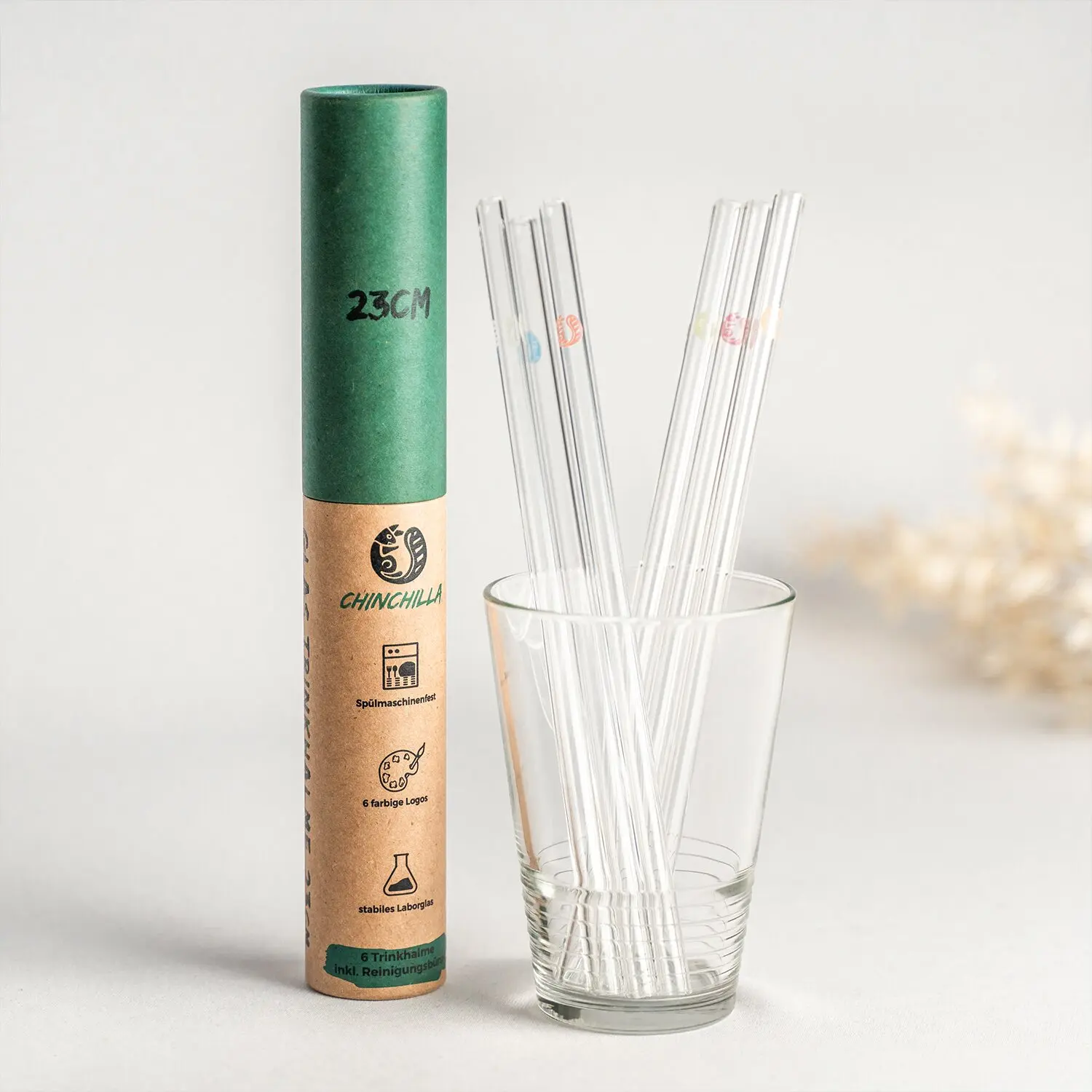 Grüne Kartonrolle mit braunem Etikett und 23 cm Aufdruck steht neben einem Glas, aus dem transparente Glastrinkhalme ragen