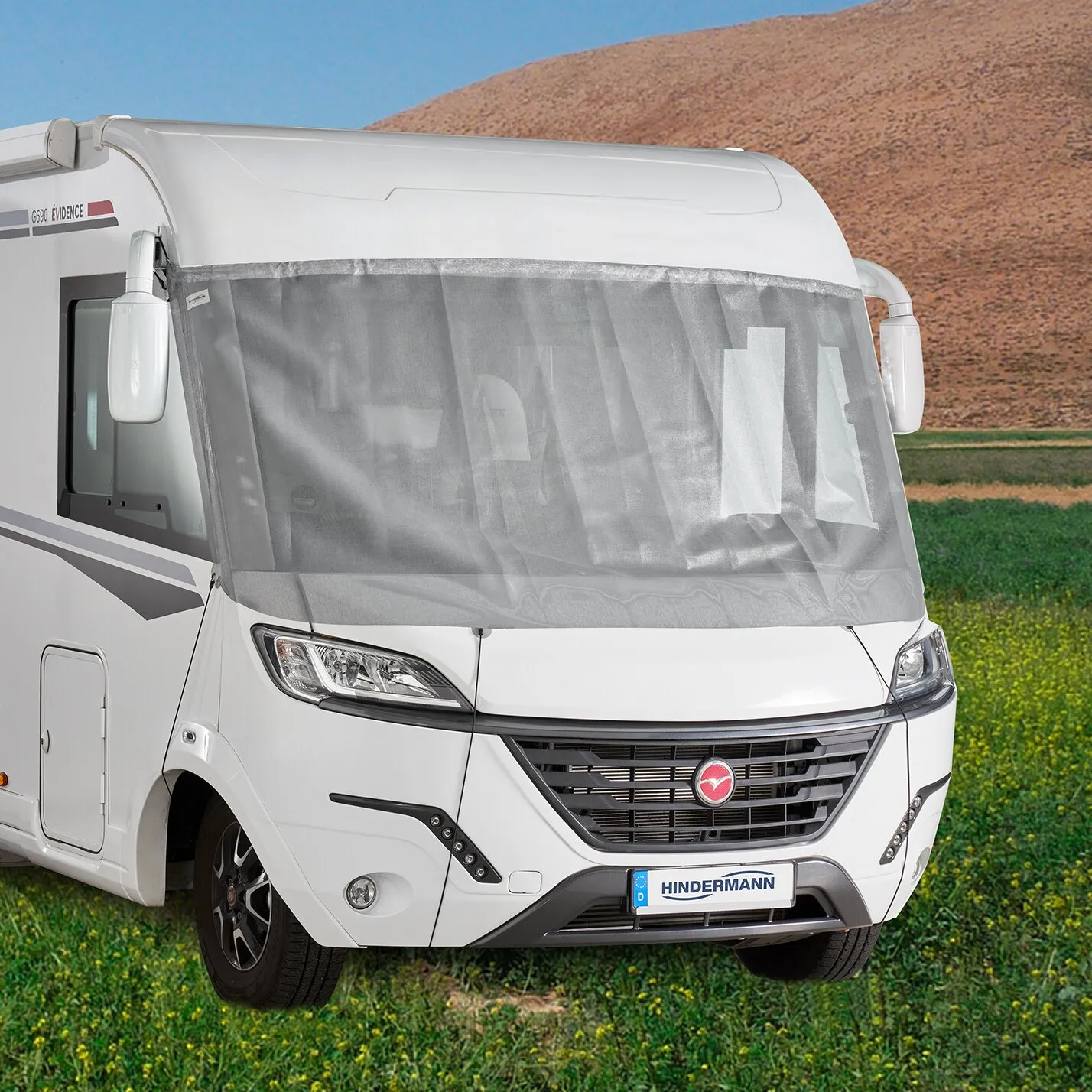 Weiße Front eines integrierten Reisemobils mit grauer Sonnenschutzmatte Screen über der Windschutzscheibe vor ländlicher Landschaft