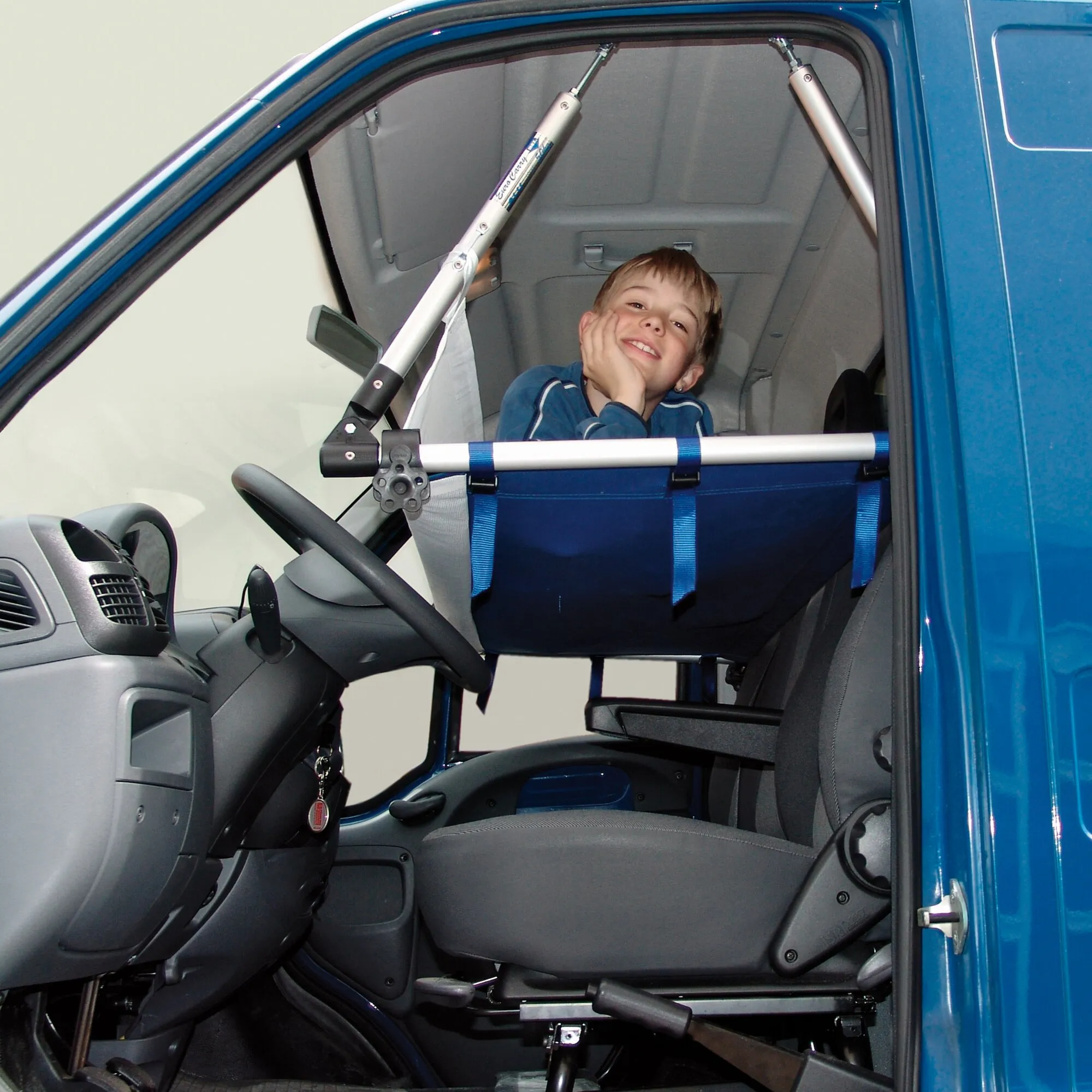 Blaues Kinderbett mit Aluminiumrahmen im Innenraum eines Autos, darin sitzt ein lächelndes Kind