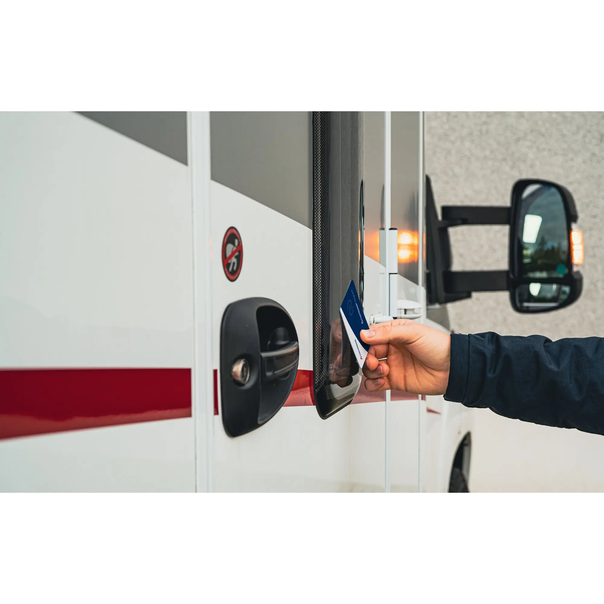 Nahaufnahme eines NFC-Moduls an der Seite eines weißen Fahrzeugs; eine Hand hält eine Karte an den Leser, im Hintergrund ist der Seitenspiegel sichtbar und ein roter Streifen zu sehen