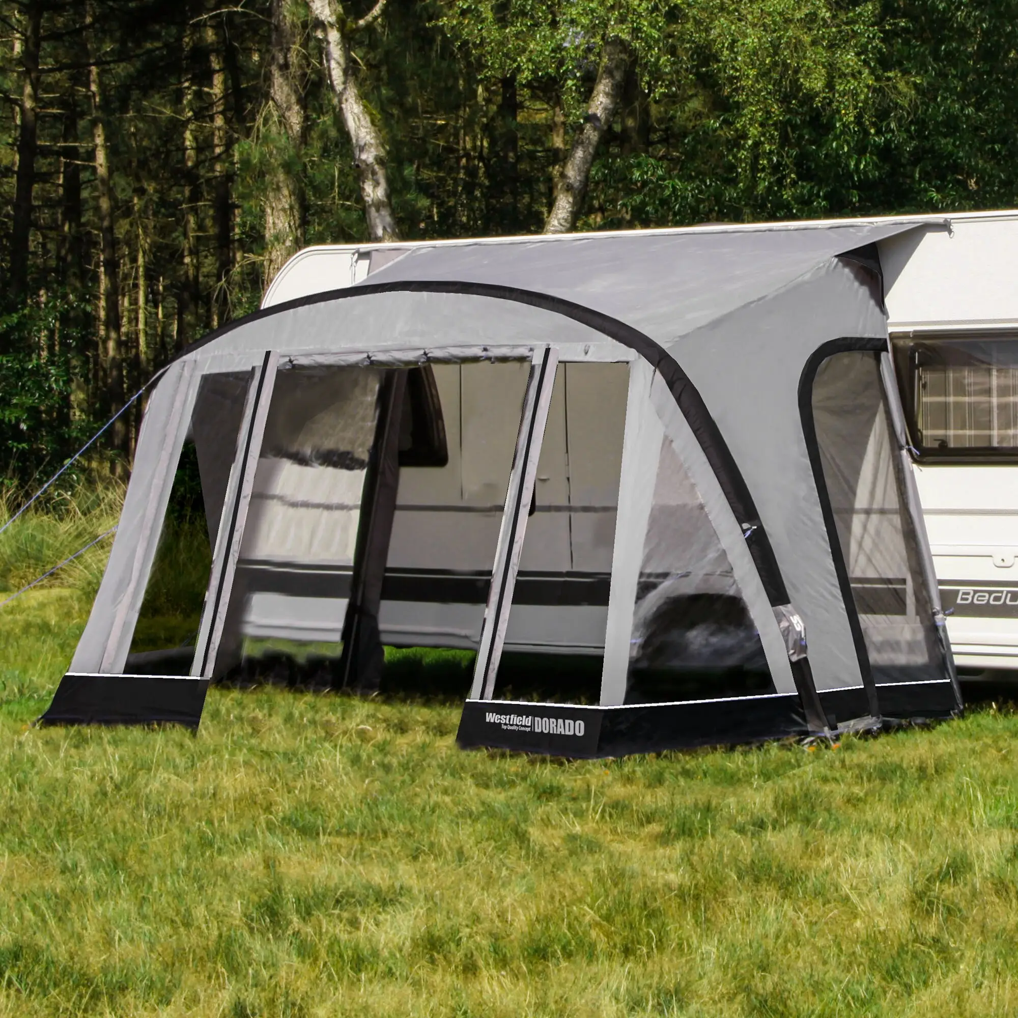 Teilzelt Dorado XL in Grau mit großen Fensterflächen und Rundbogenfront, am Wohnwagen angebaut, Gras und Wald im Hintergrund