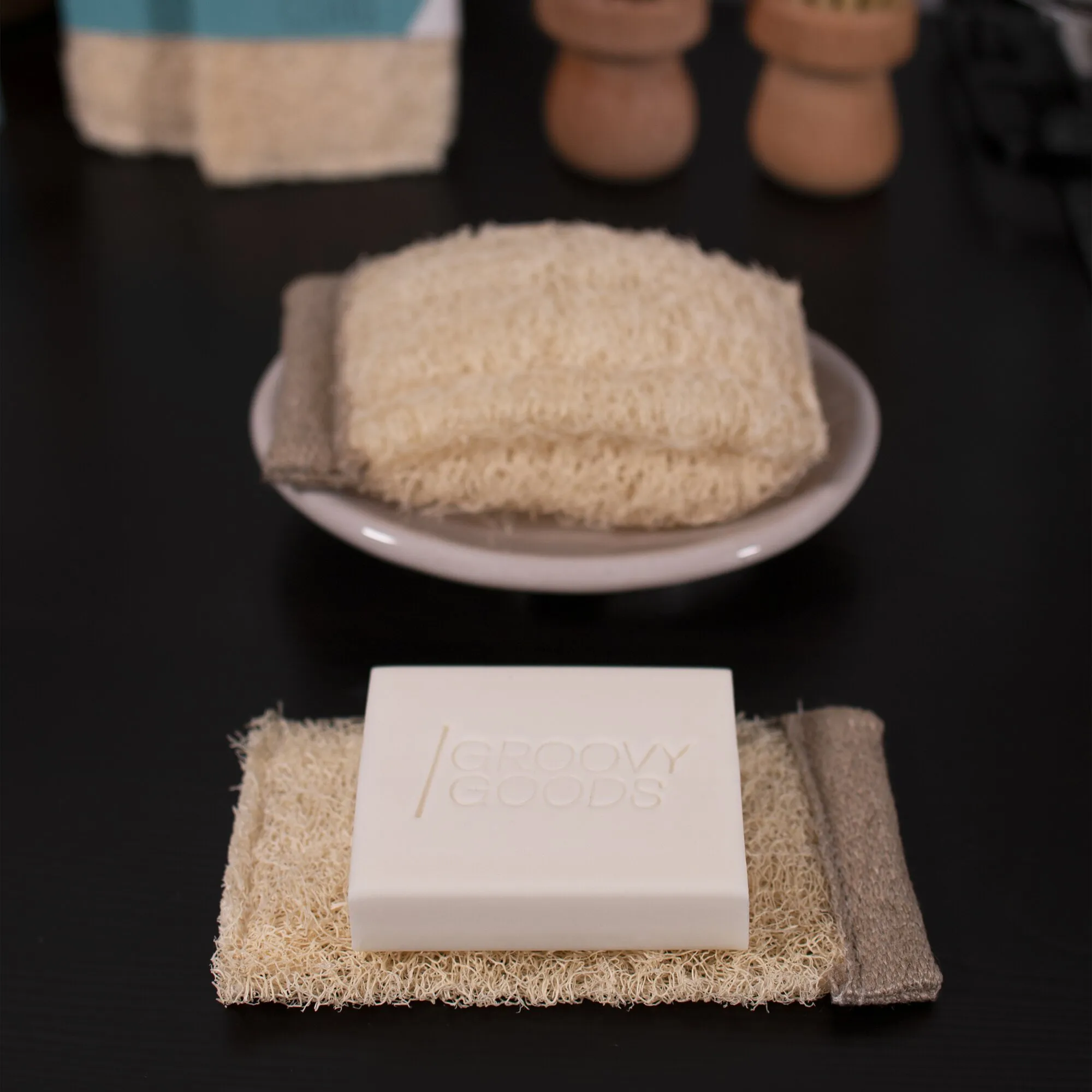 Clearo Luffa-Schwamm und Ablage mit festem, weißem Reiniger auf naturfarbenem Luffa-Material neben einer Keramikschale