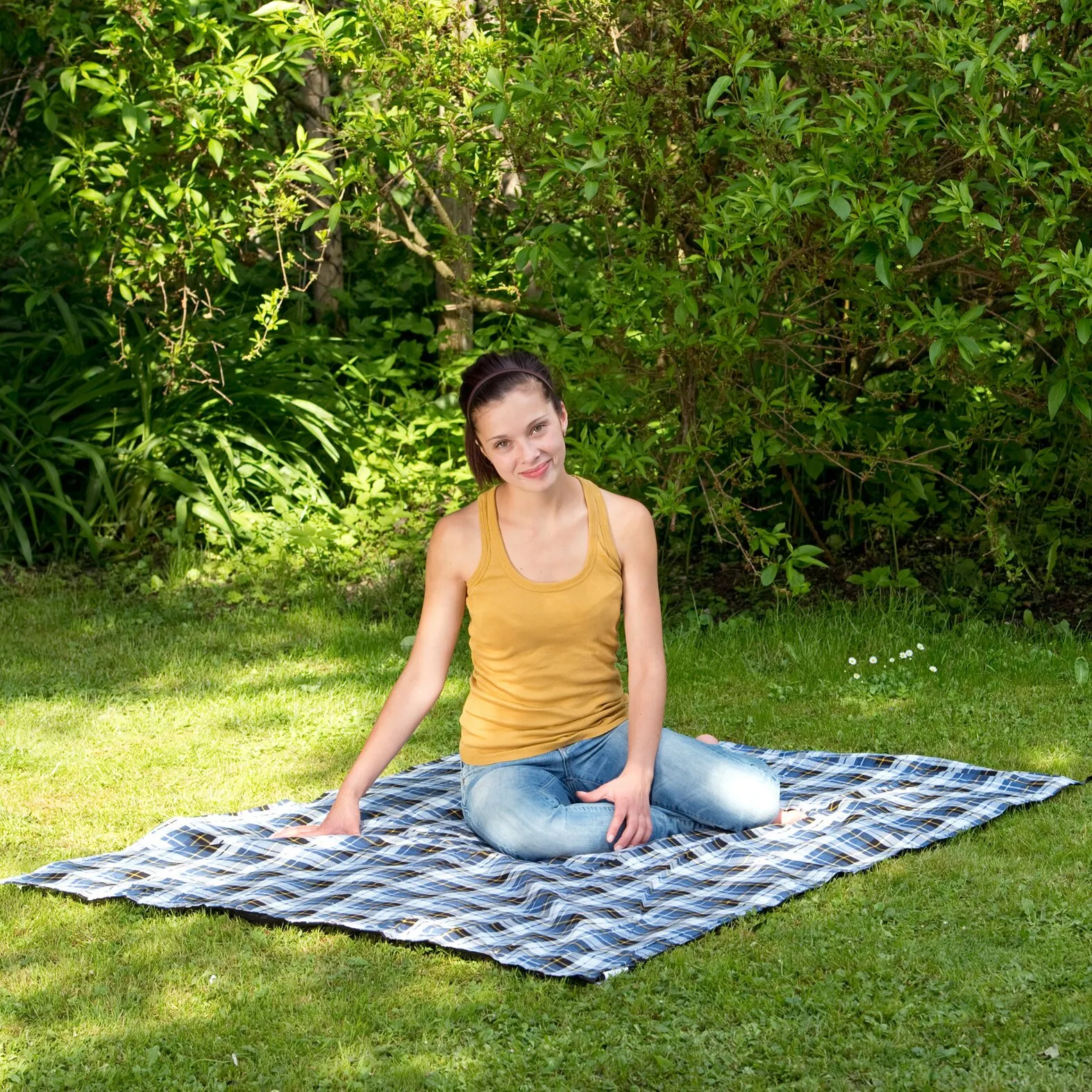 Frau sitzt auf der blau-weiß karierten Picknickdecke Ultra-Light im Gras eines Gartens
