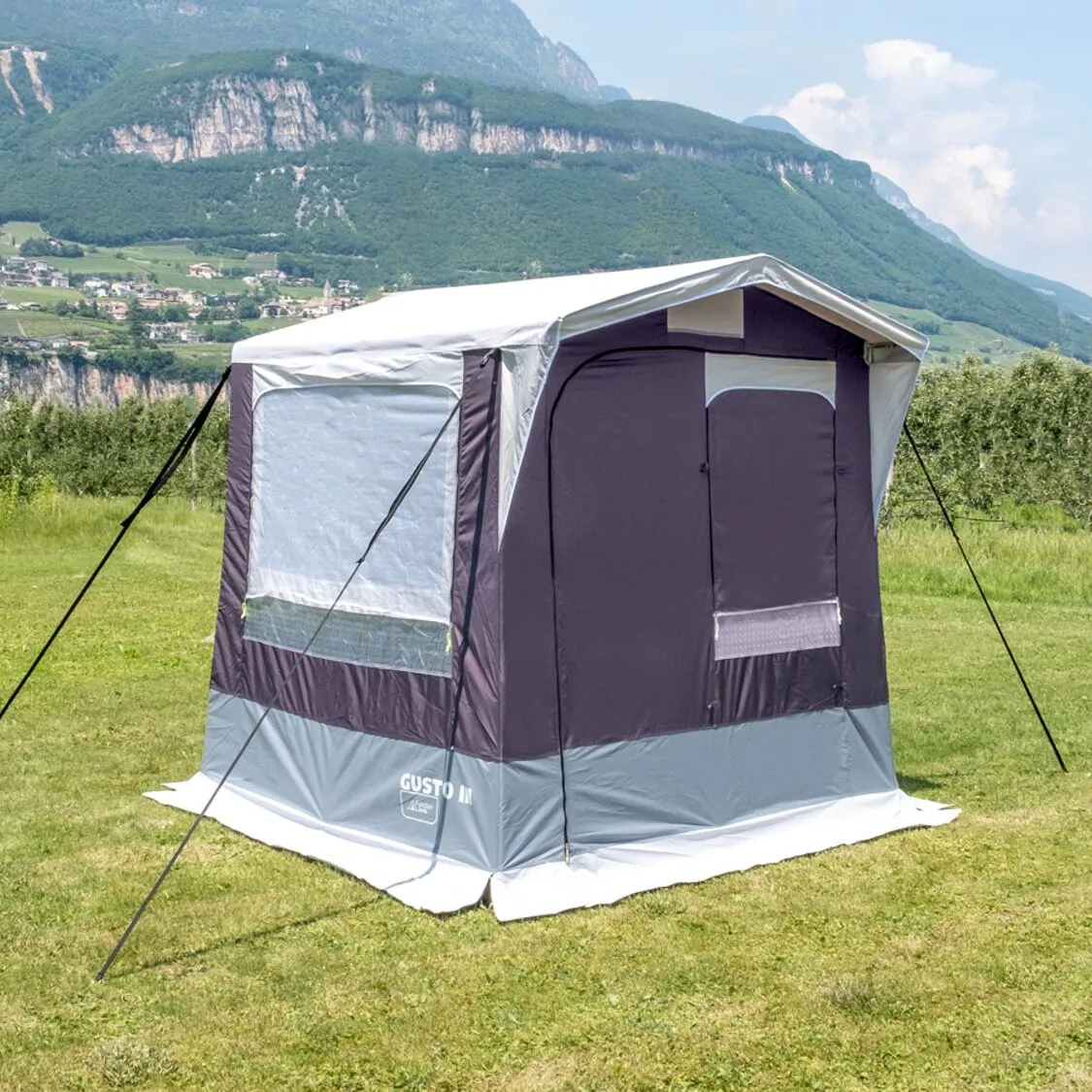 Dunkelgraues Küchenzelt Gusto II NG mit Fenstern und Abspannleinen auf einer Wiese vor einer Berglandschaft