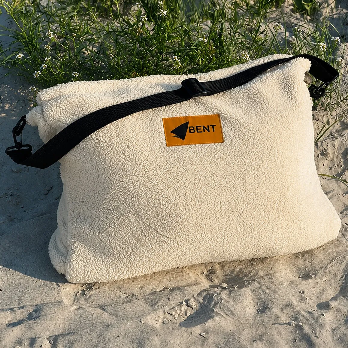 Cremefarbener Vanlife-Schlafsack Bentcho im Leo-Design mit schwarzem Tragegurt und orangefarbenem BENT-Logo im Sand liegend