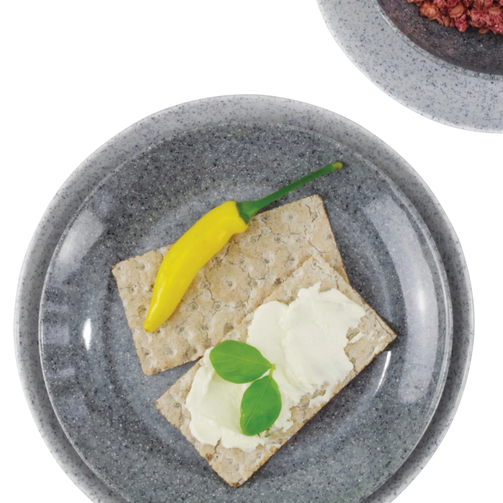 Granitgrauer runder Teller des Geschirrsets Solid Line mit Knäckebrot, Frischkäse, Basilikumblättern und gelber Paprika belegt