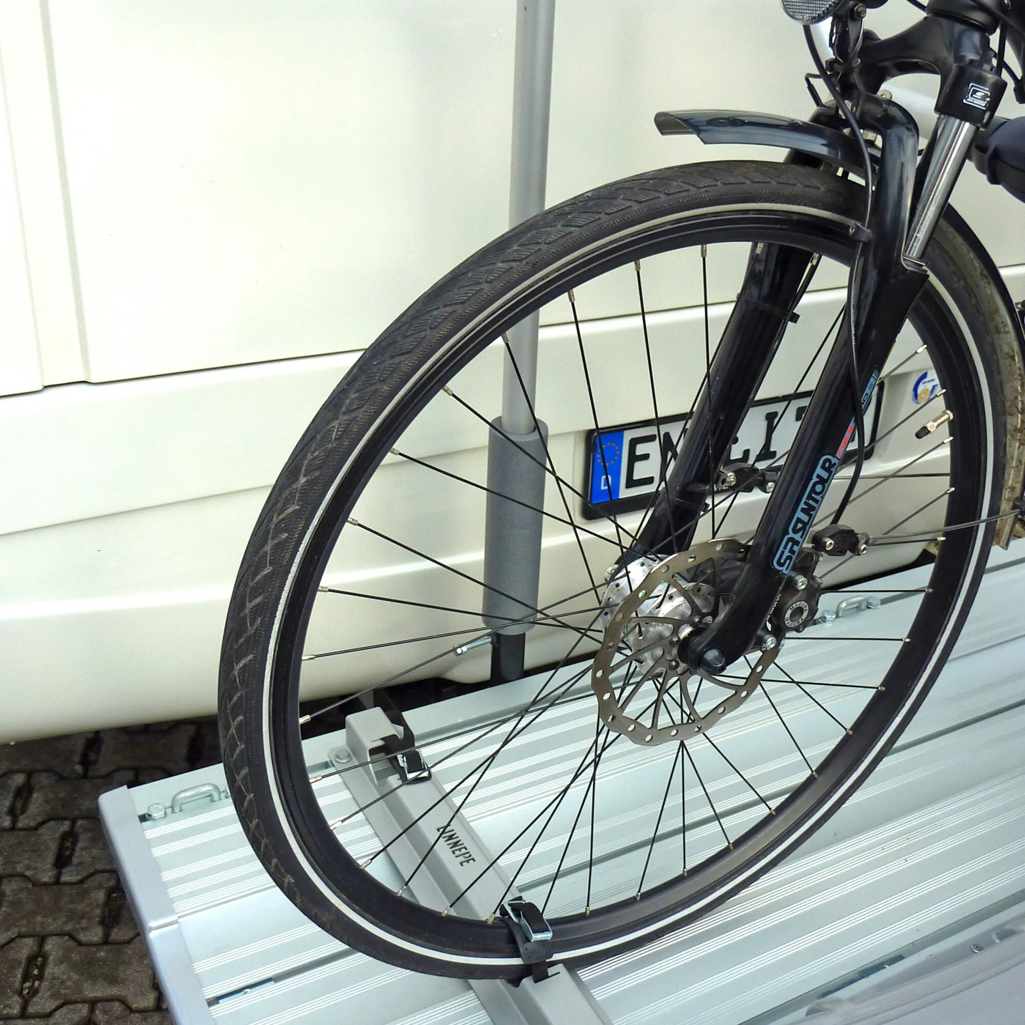Schwarzes Fahrrad auf einem silbernen SlidePort-Lastenträger, gesichert mit Radschienen und Haltegurten des Basic-Fahrradhalters