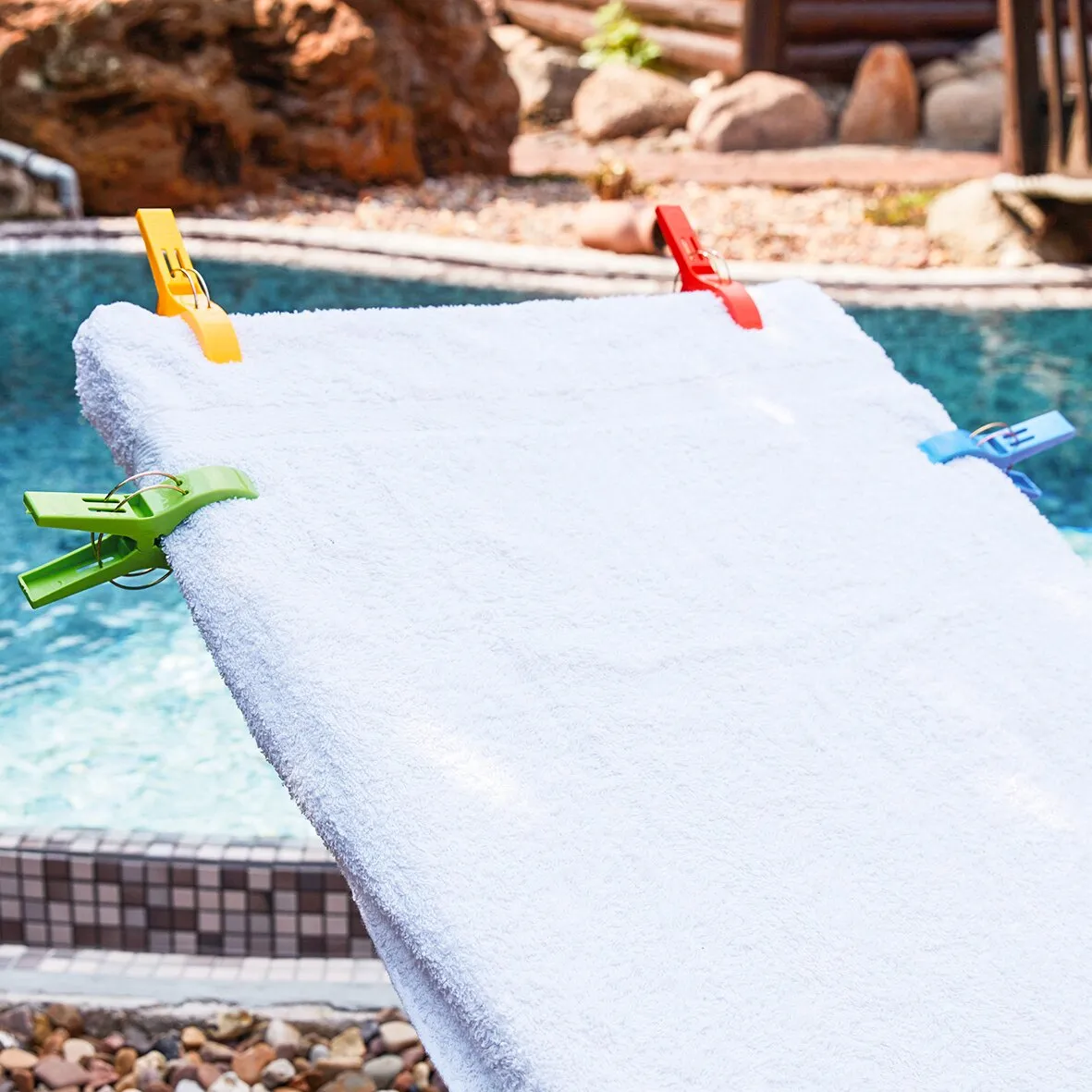 Weißes Strandhandtuch, mit bunten Handtuchhaltern am Rand an einem Pool befestigt
