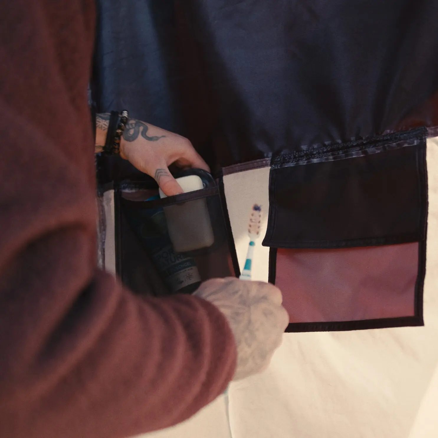 Hände mit Tattoos greifen in einen Taschen-Organizer des Horizon Duschzelt ohne Boden; Zahnbürste, Flasche und Pflegeartikel sichtbar