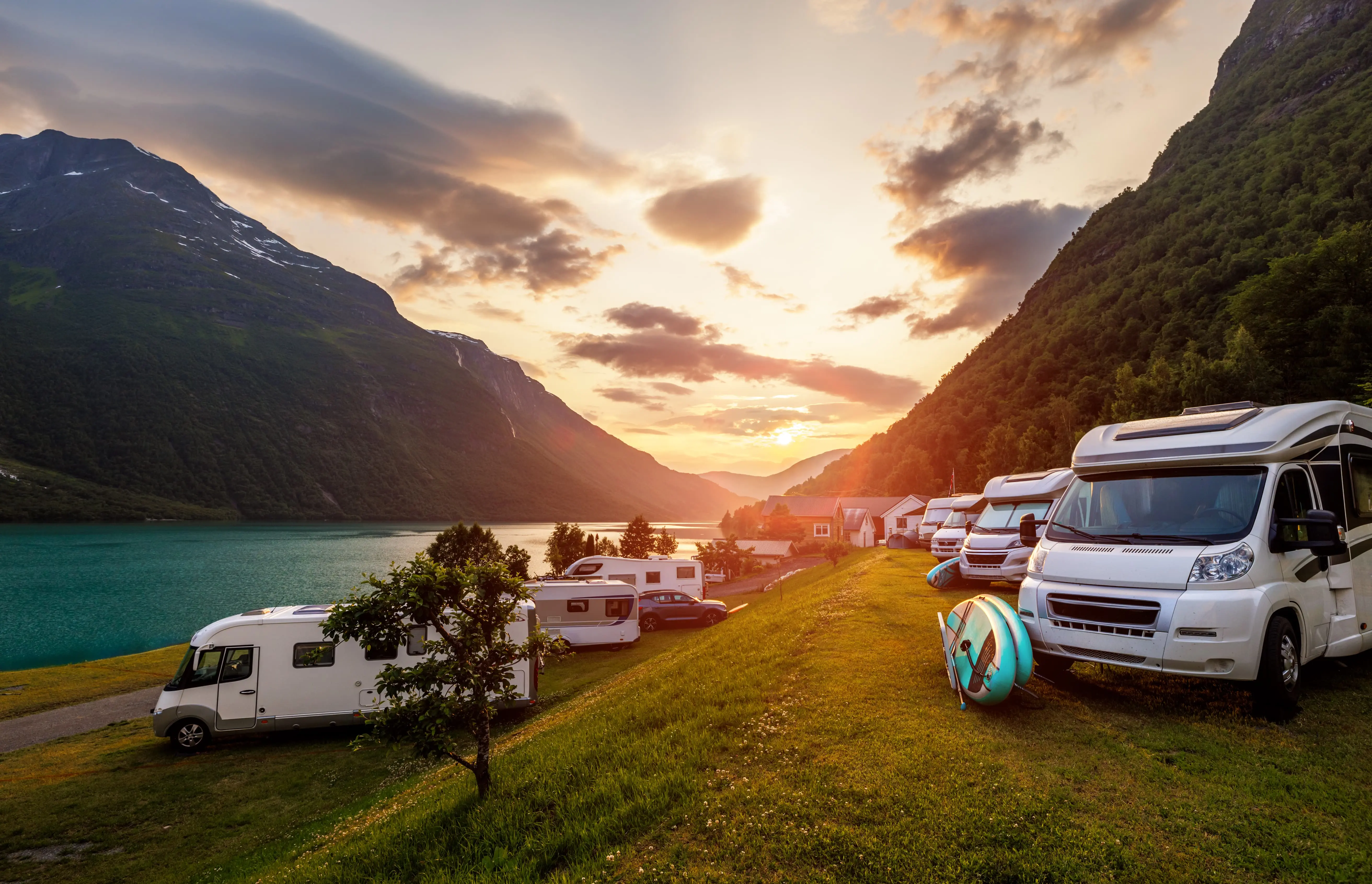 Sonnenuntergang über dem Fjord; mehrere Wohnmobile am Ufer, vorderes Reisemobil mit Solarpanel; ein Schwimmring liegt daneben