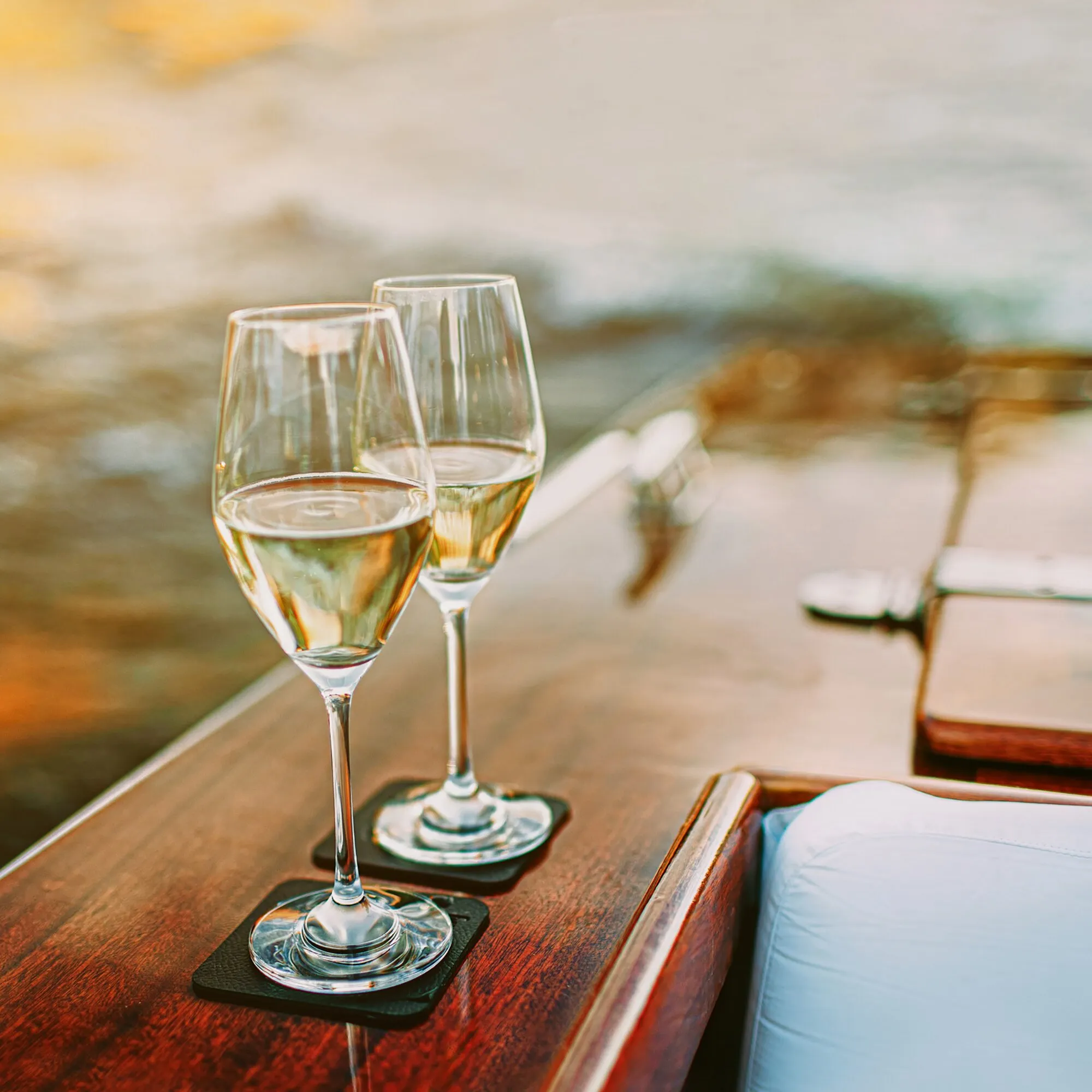Zwei transparente Kristallgläser mit Stiel und goldenem Champagner auf schwarzen Untersetzern an einem gedeckten Tisch