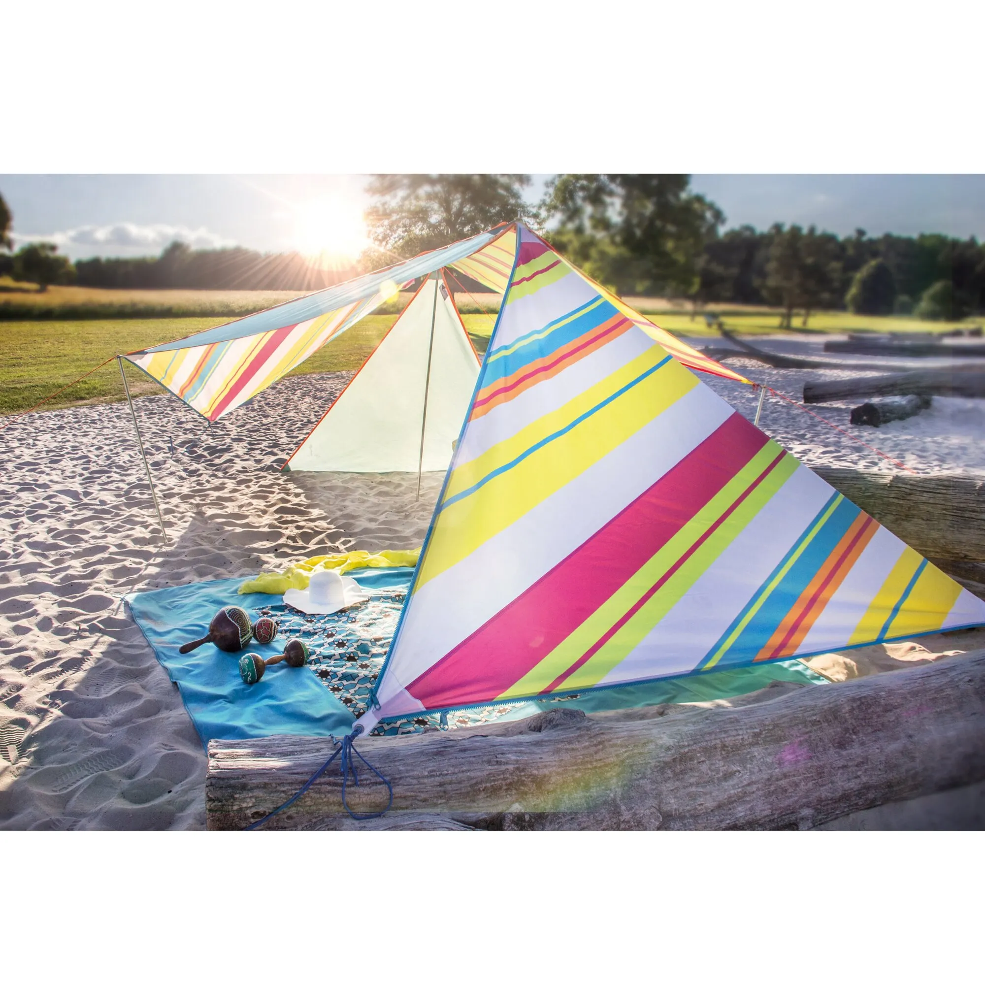 Farbenfrohes Sonnensegel Zip Canvas Caribbean mit Hawaii-Streifen, aufgespannt am Sandstrand neben einer Picknickdecke und Musikinstrumenten