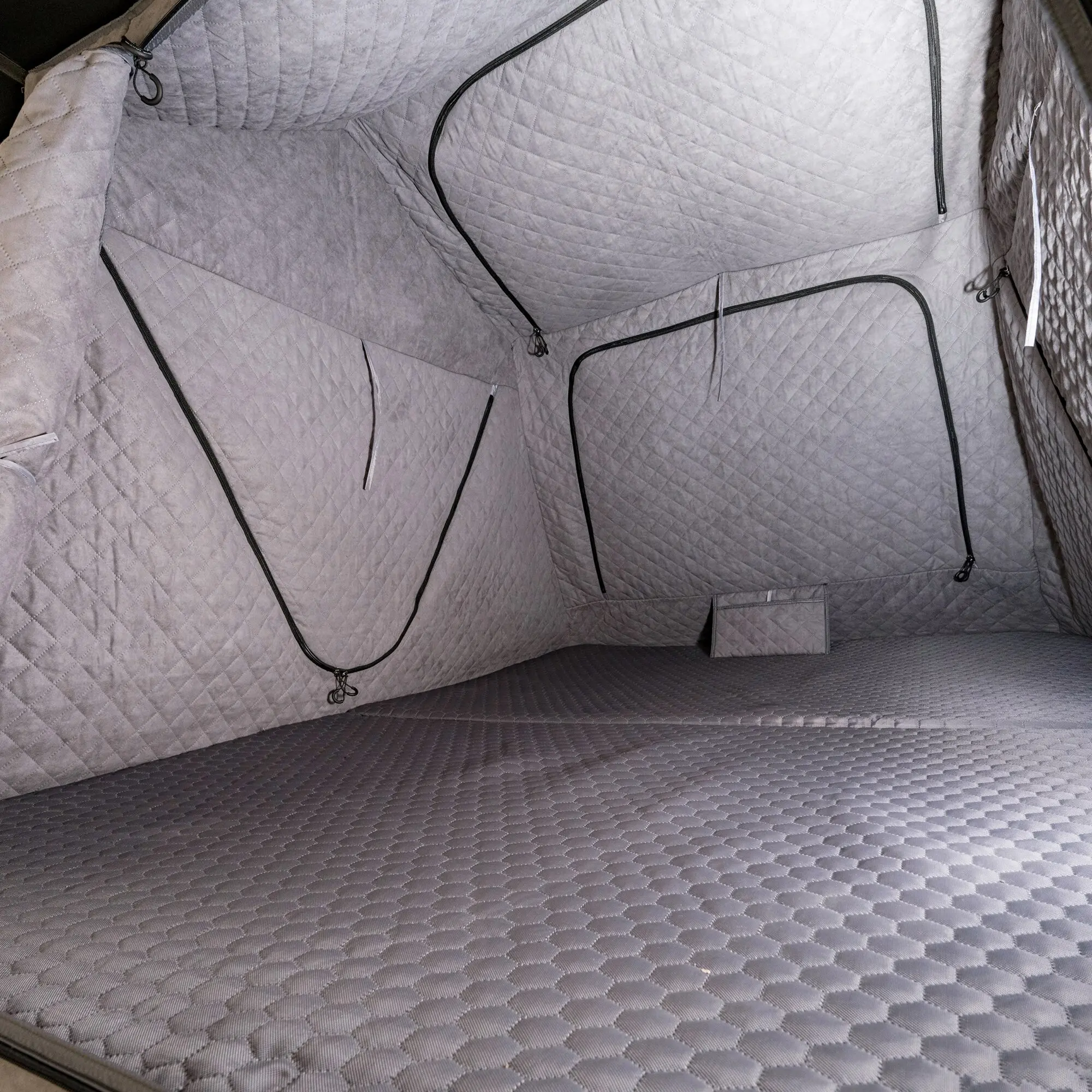 Innenraum eines grauen gequilteten Thermo-Innenzelts für Roof Space 4, mit schwarzen Reißverschlüssen, Zugschnüre und Haken seitlich