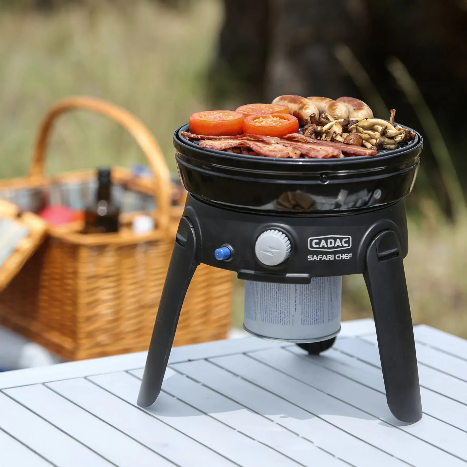 Schwarzer CADAC Safari Chef Campinggrill mit aufgeschraubter Gaskartusche, darauf grillen Tomaten, Speck, Pilze und Würstchen