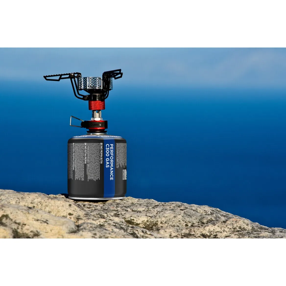 Schwarze Gaskartusche Coleman Performance C300 Gas mit aufgesetztem Campingkocher auf einem Felsen vor blauem Himmel
