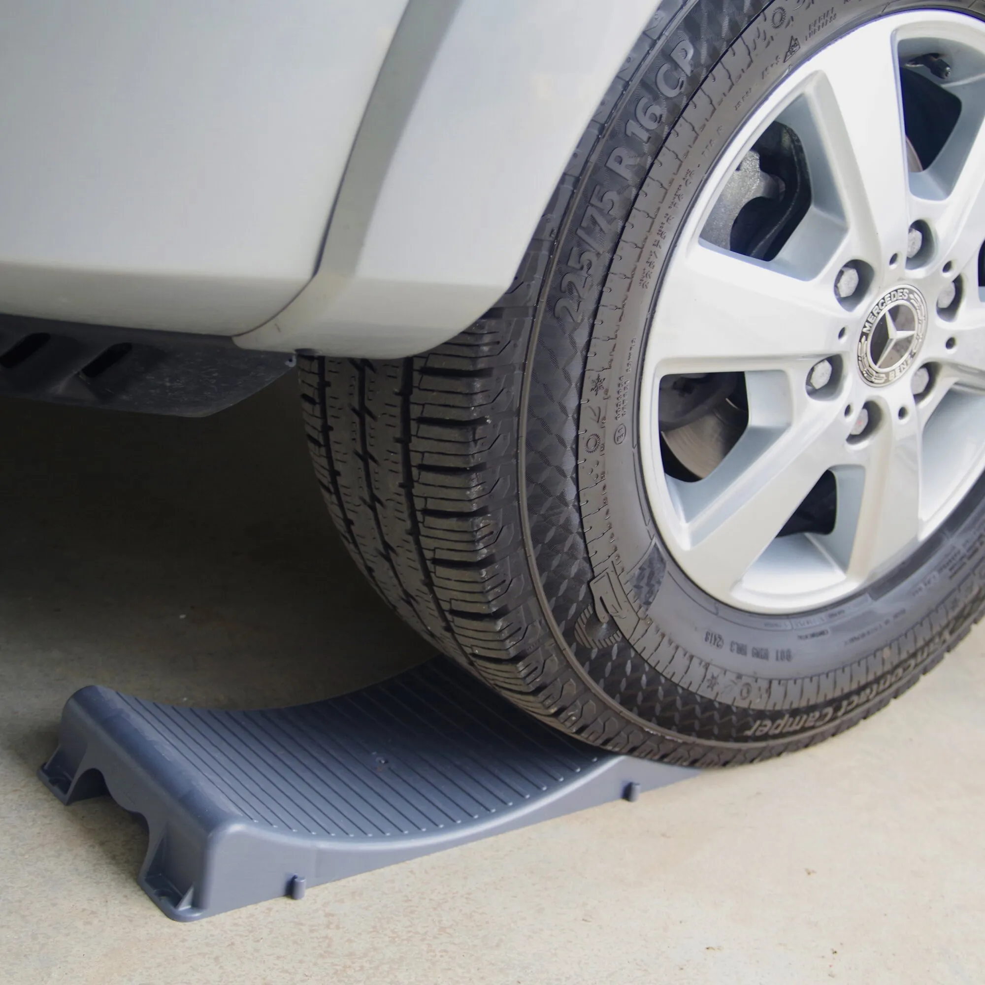 Dunkelblauer Unterlegkeil Wheel Saver unter dem Reifen eines Mercedes-Fahrzeugs zur Sicherung gegen Wegrollen