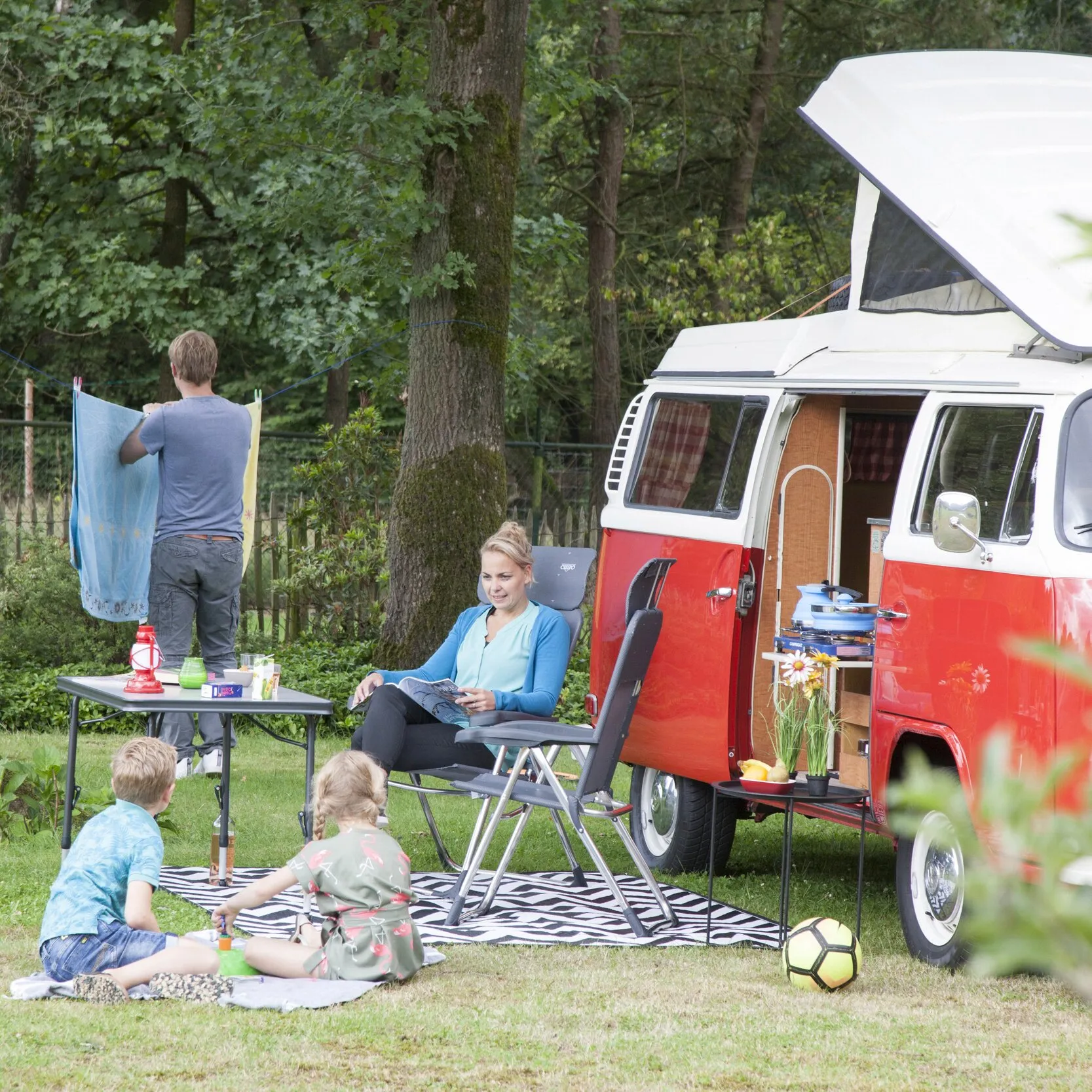 Campingstuhl AL/213 Classic mit grauer Sitzfläche und Armlehnen, von einer Frau beim Camping neben einem Wohnmobil genutzt