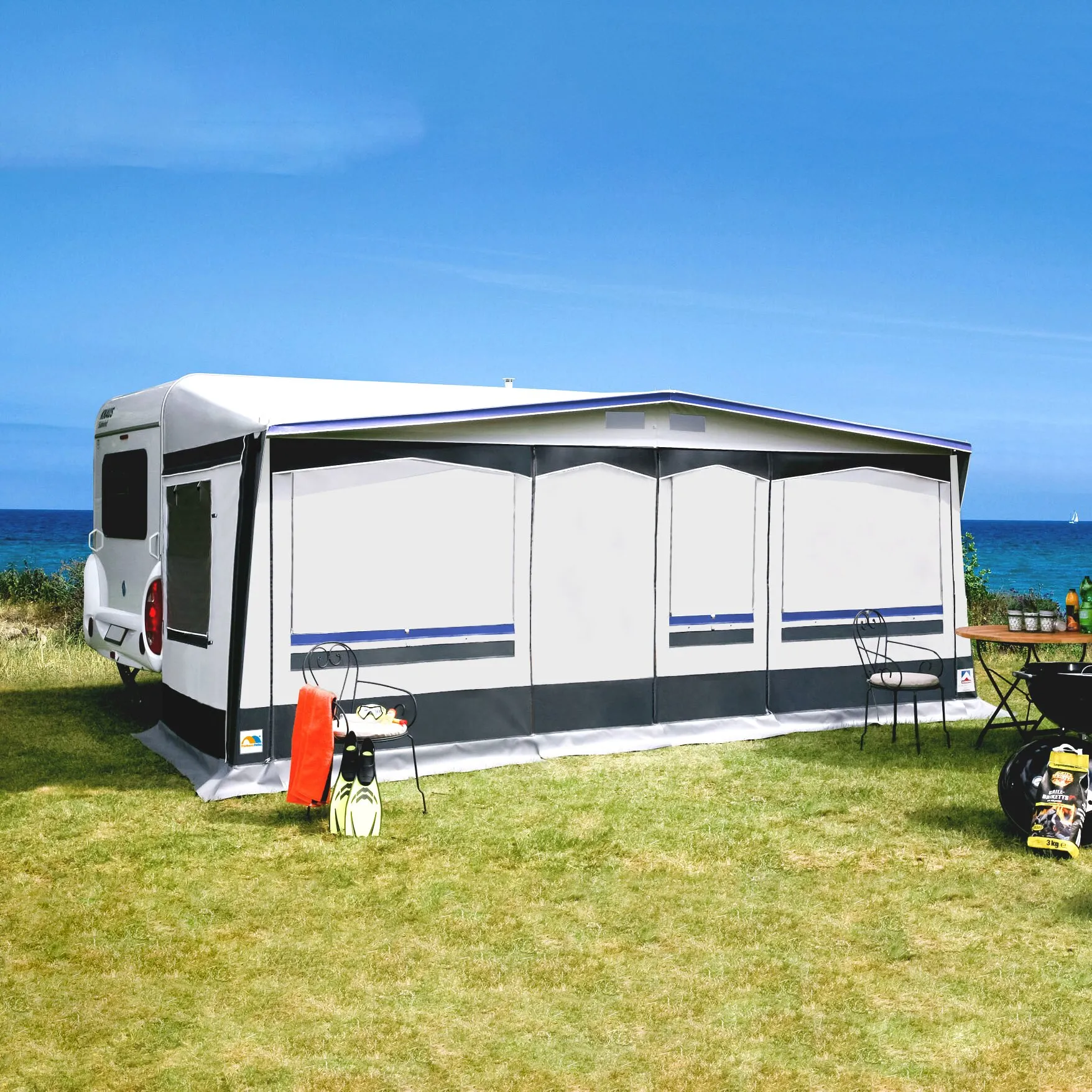 Saisonvorzelt Prestige in Weiß und Grau am Wohnwagen, mit mehreren Frontfenstern und Sitzbereich auf einer Wiese am Meer