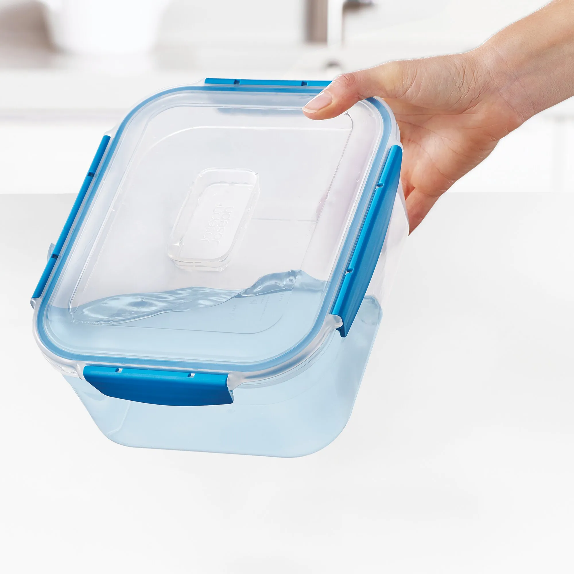 Transparente rechteckige Vorratsdose des Sets Nest™ Lock mit blauem Deckel und Verschlussclips, von einer Hand gehalten