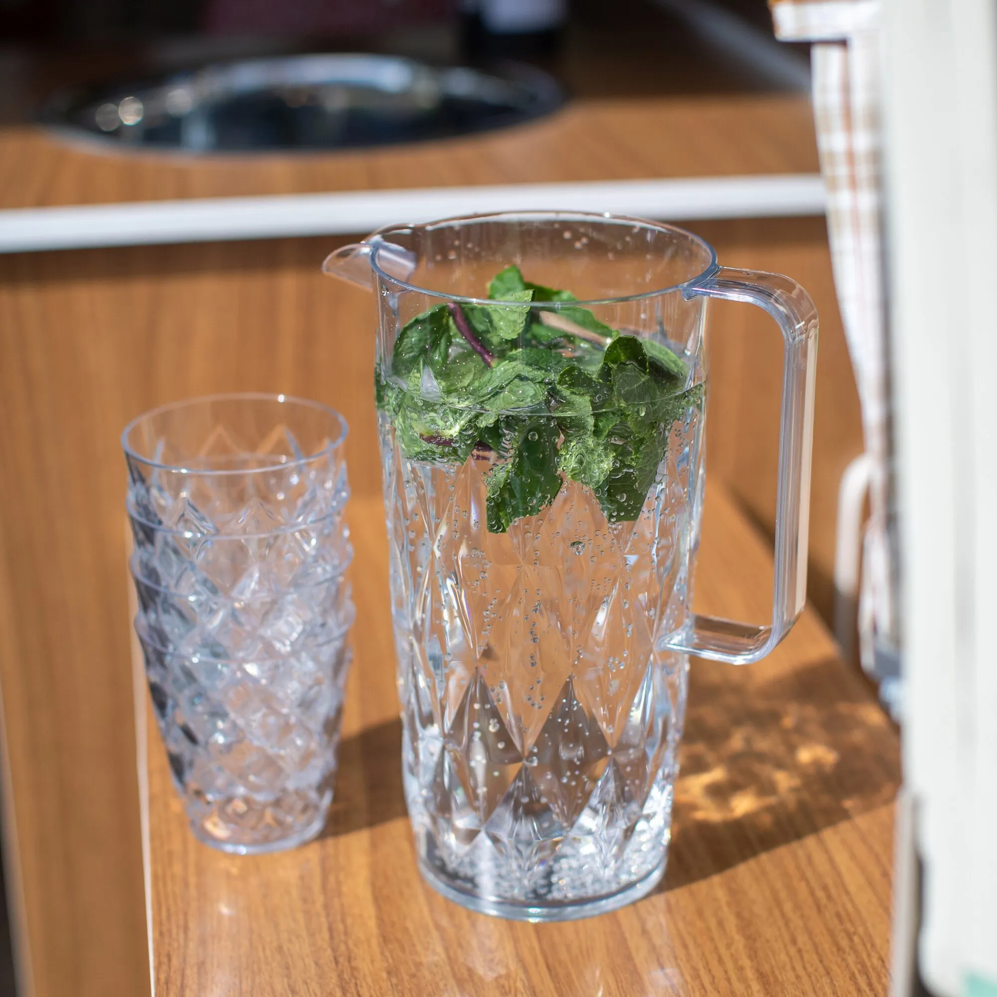 Transparente Kanne CRYSTAL mit facettiertem Muster, Minzwasser und einem passenden Becher auf einem Holztisch