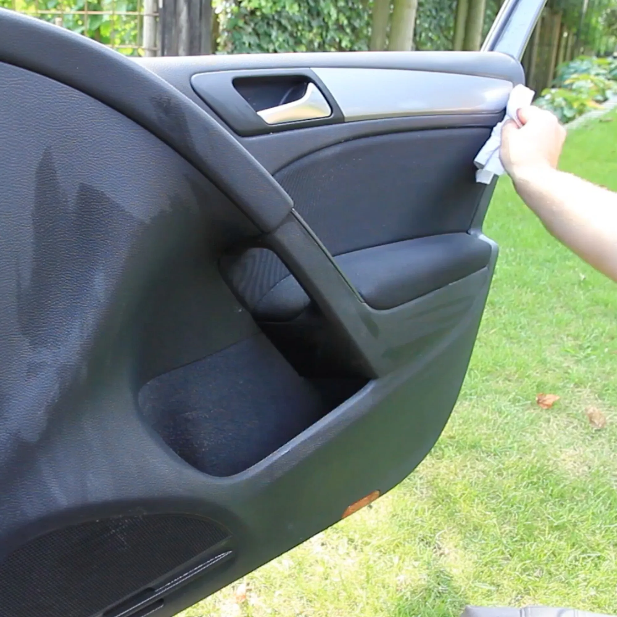 Hand wischt mit einem Tuch die schwarze Innenverkleidung einer geöffneten Autotür mit Schaumreiniger MULTICLEAN ab