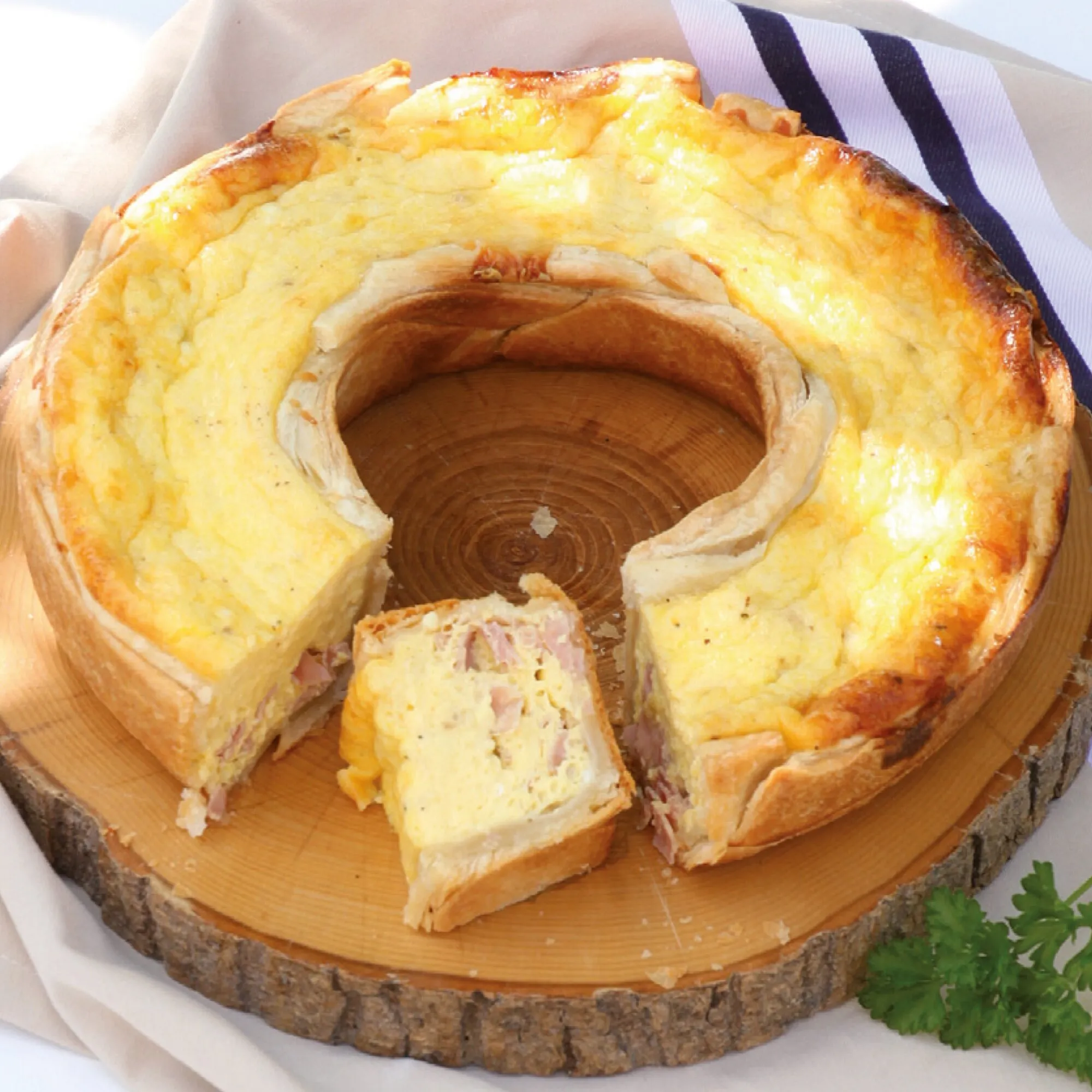 Aufgeschnittener, goldbraun gebackener herzhafter Ringkuchen mit Schinkenfüllung auf einem rustikalen Holzbrett, passend zum Omnia-Backofen-Kochbuch