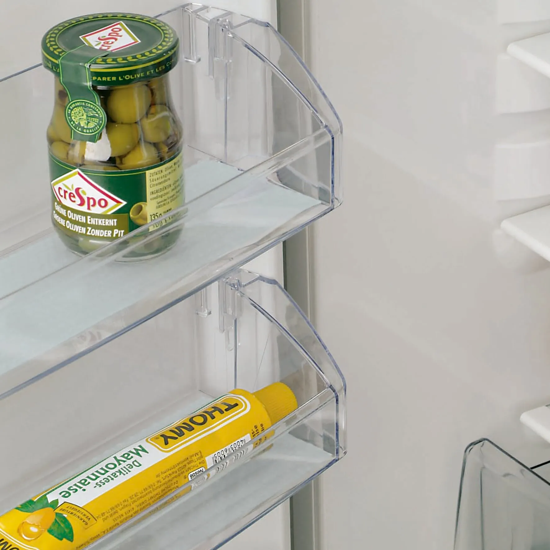 Transparente Kühlschrankfächer mit Antirutschfolie Cool & Fresh, darauf ein Olivenglas und eine gelbe Mayonnaise-Tube