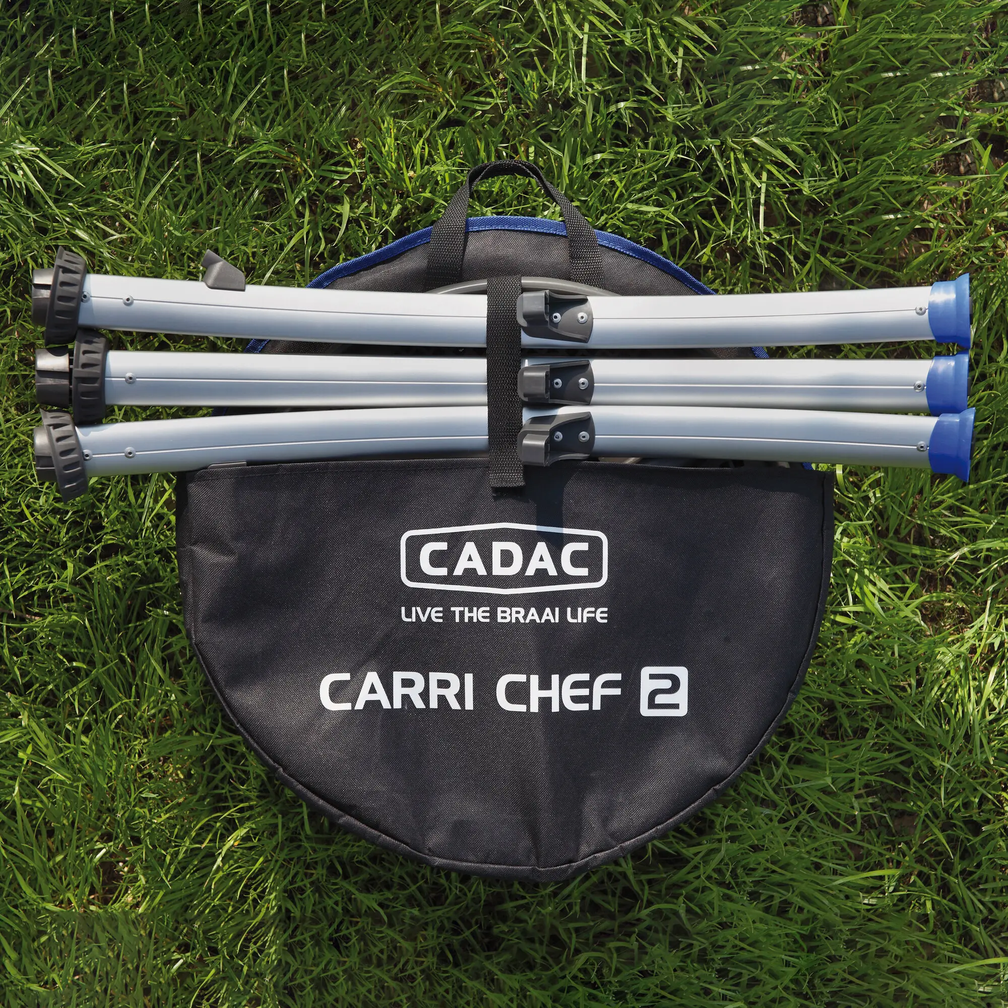Zusammengelegte graue Aluminium-Beine des Carri Chef 2 Grills liegen in einer schwarzen CADAC Tragetasche mit Griffen, Gras im Hintergrund