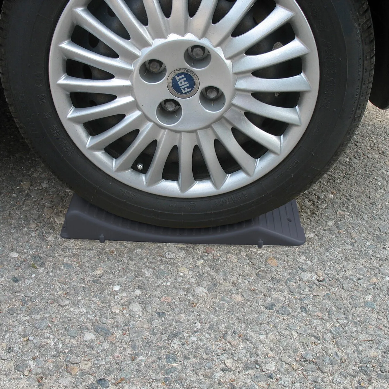 Schwarzer Unterlegkeil Wheel Saver sichert ein Fiat-Autoreifenrad auf grobem Asphalt