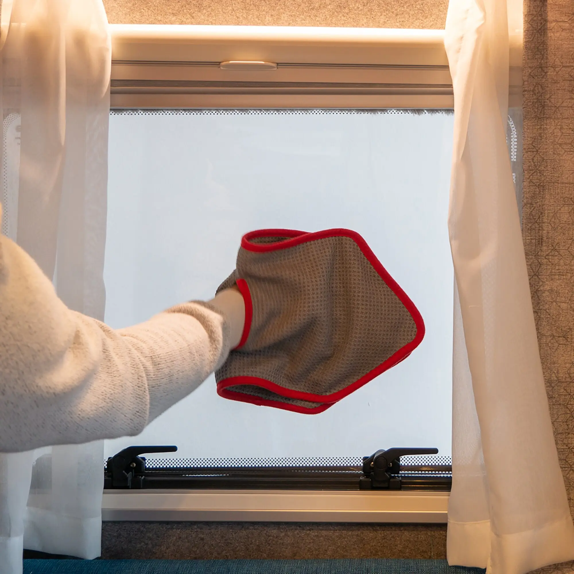 Braunes Mikrofasertuch Grip Cut Waffle mit roter Umrandung, getragen wie ein Handschuh an der Hand vor einem Fenster mit hellen Vorhängen