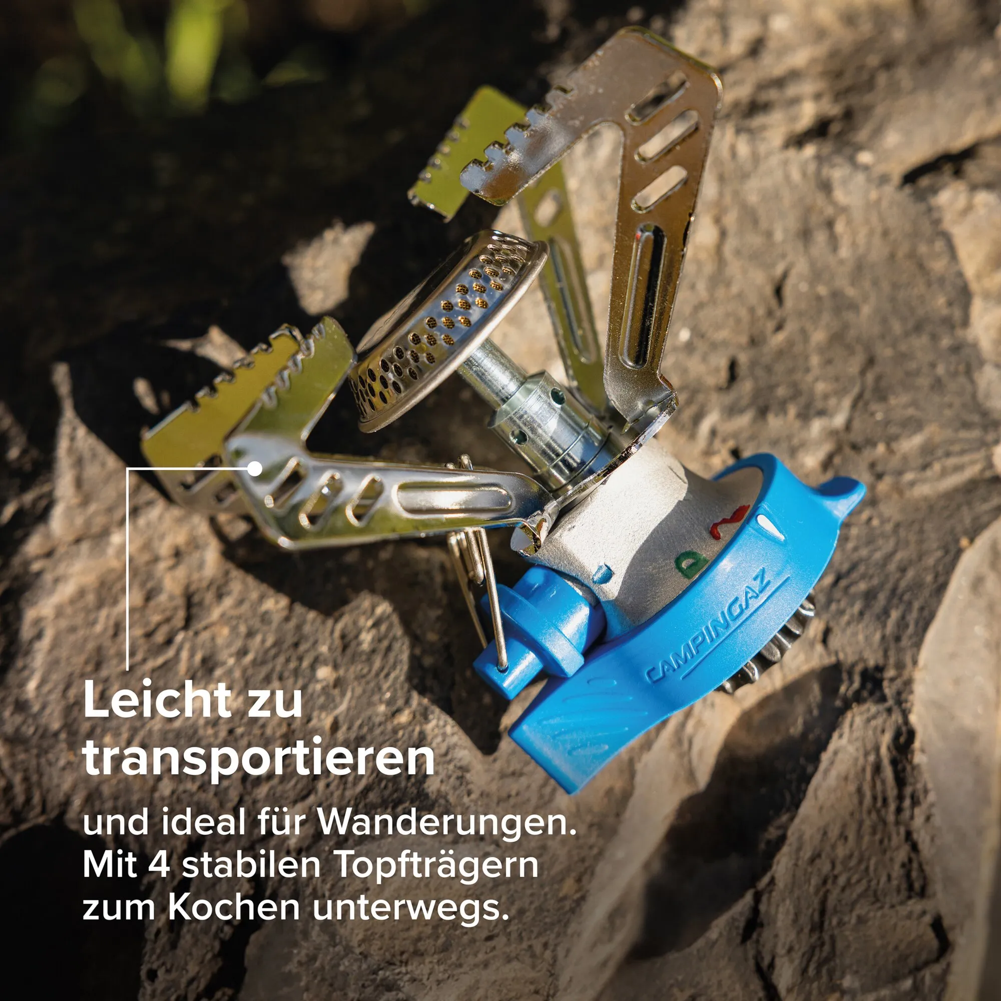 Nahaufnahme eines Campingkocher-Systems mit faltbaren Topfträgern aus Metall, perforierter Brennerplatte, olivgrünen Rahmenteilen und blauem Griff