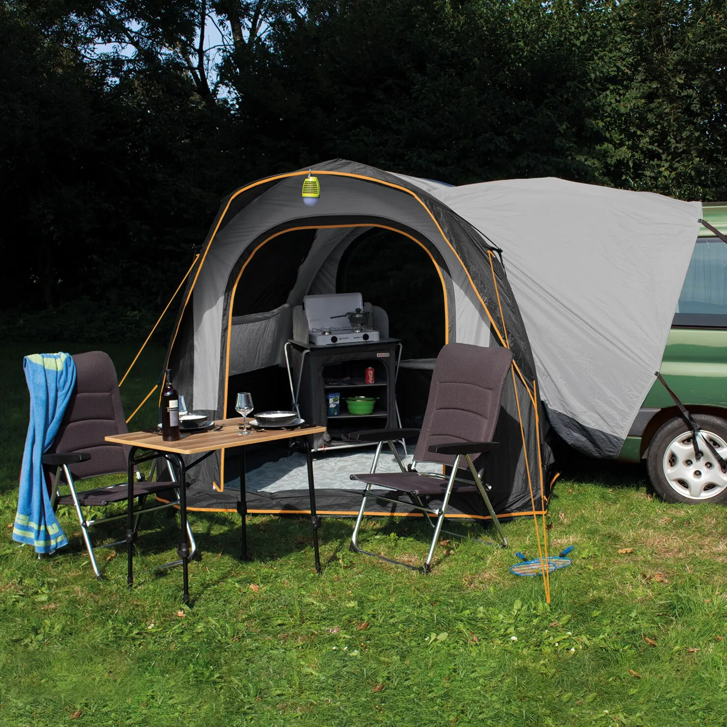 Graues Heckzelt Cruiser SUV Air mit orangefarbenen Nähten am Fahrzeug, eingerichtet mit Campingtisch, Stühlen und Kochausrüstung